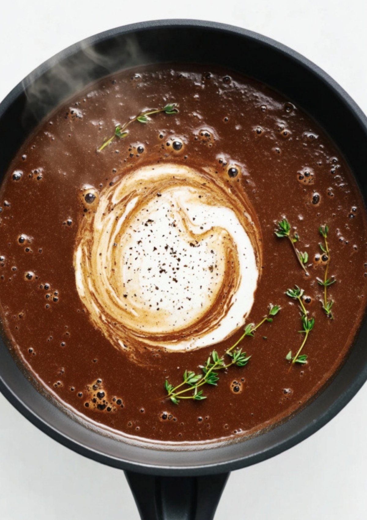 Pan of Marsala wine sauce with a swirl of heavy cream and fresh thyme, ready for veal scallopini.