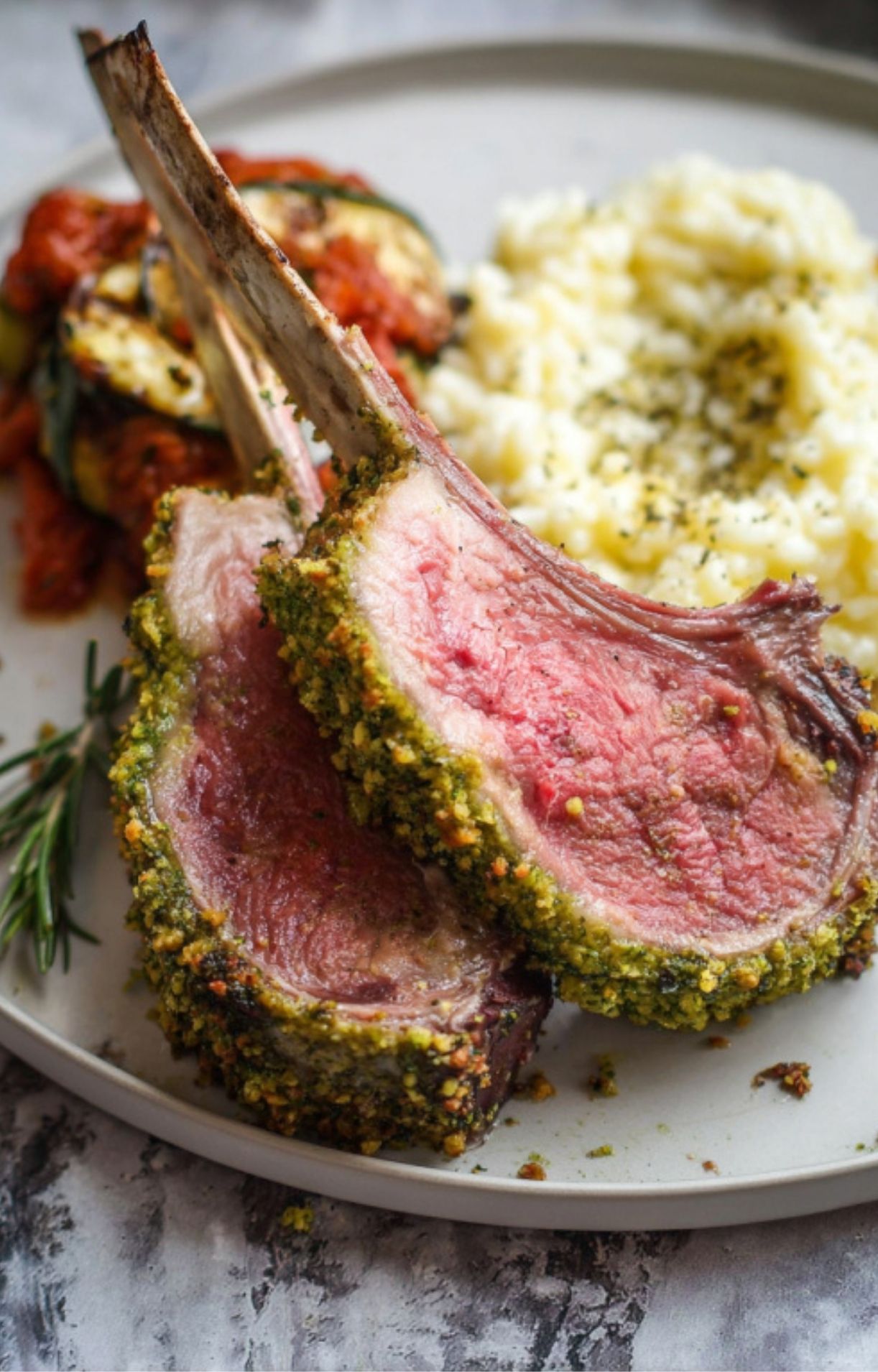 Two herb crusted lamb chops served with creamy risotto and roasted vegetables on a plate