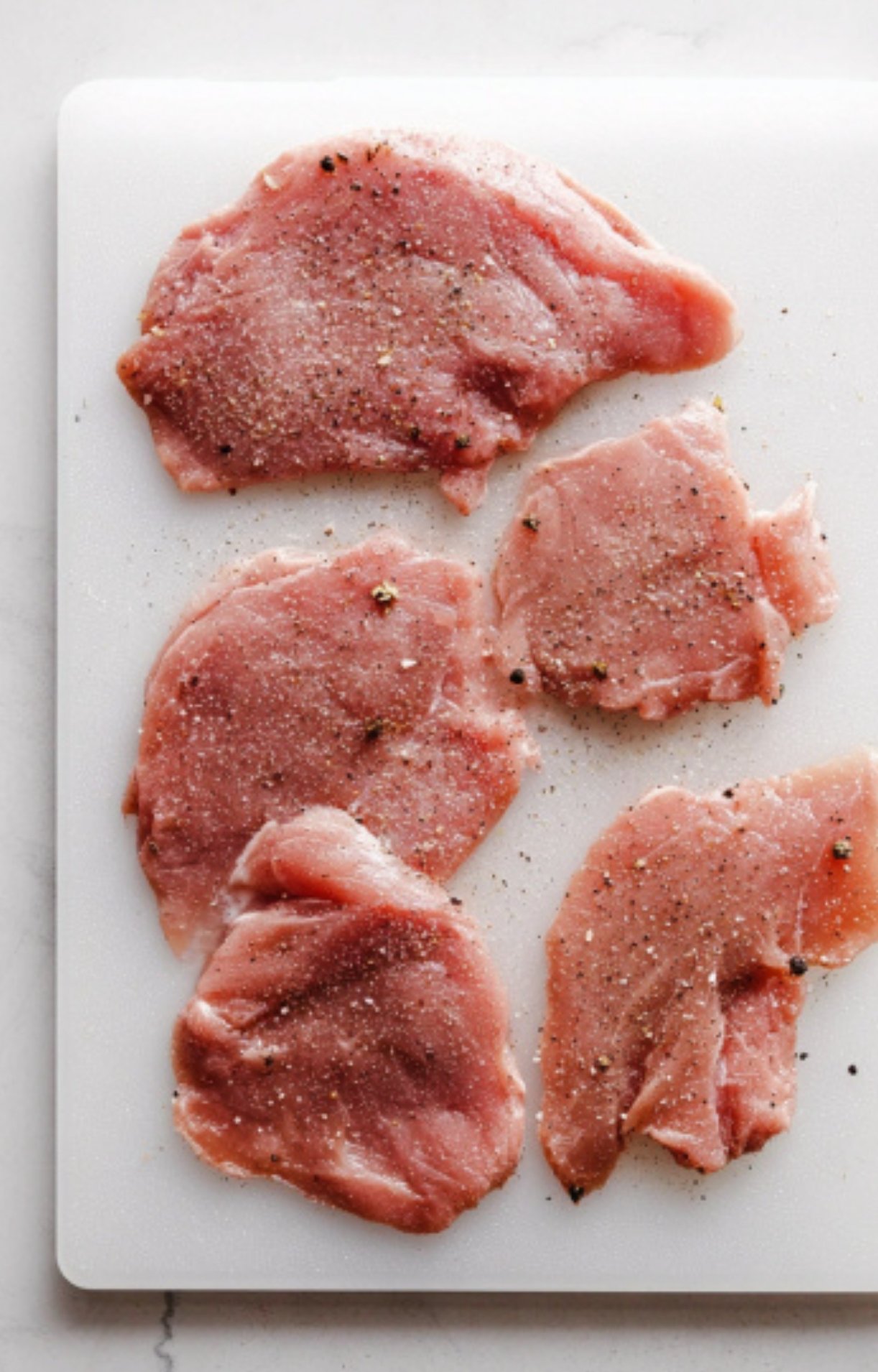 Raw veal cutlets seasoned with salt and pepper, ready to be breaded for veal scallopini Milanese recipe.