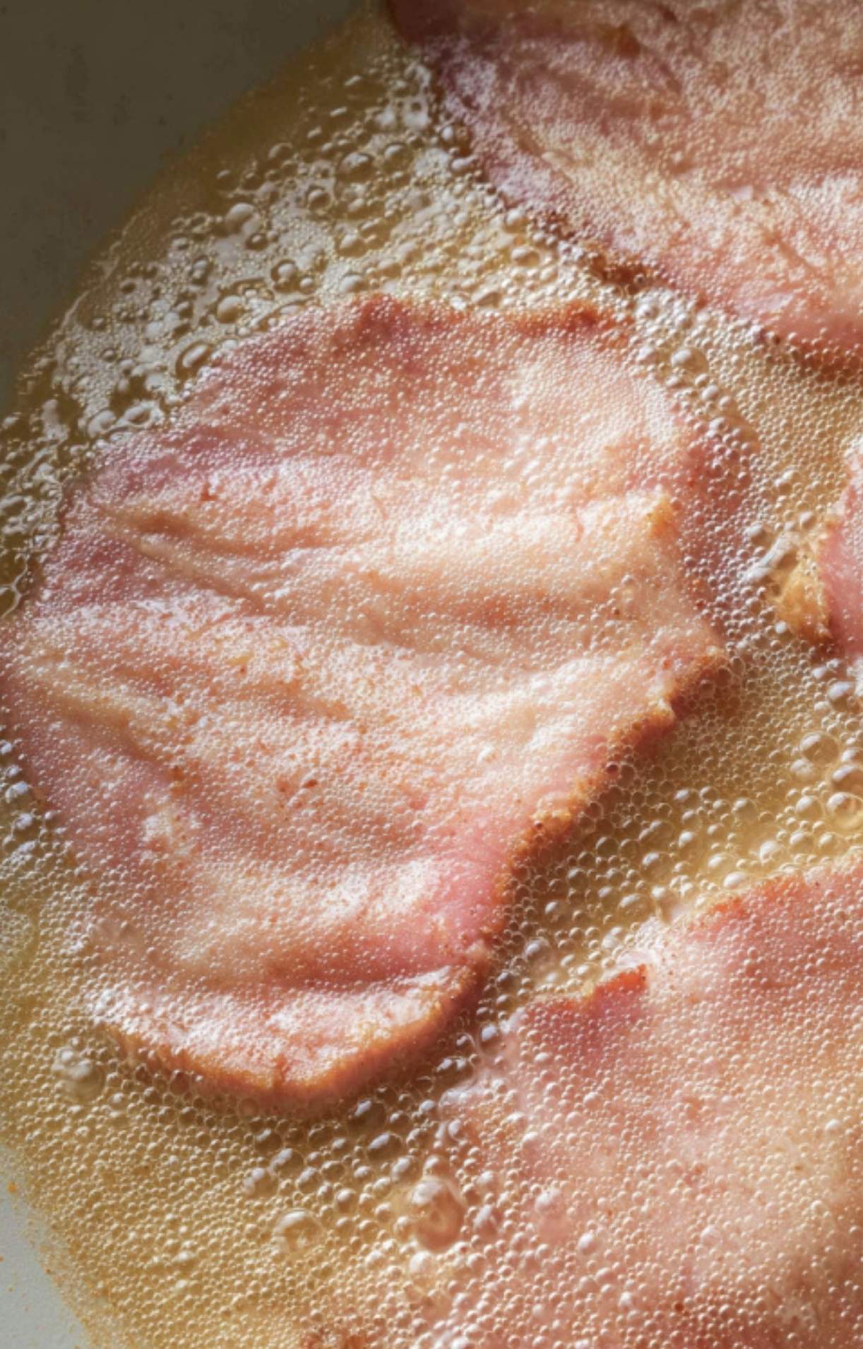 Close-up of thin veal slices beginning to sizzle in a hot pan with oil to create Veal Scallopini in Lemon Sauce.