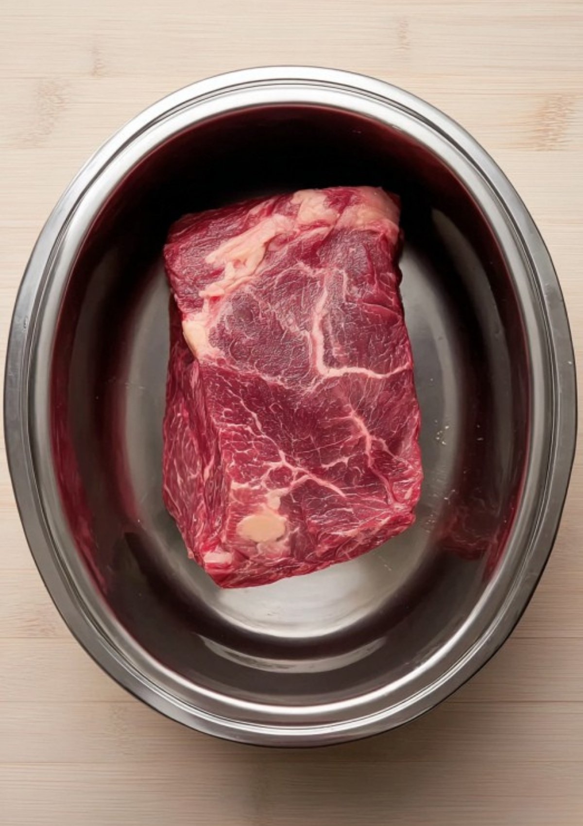 Raw corned beef brisket placed in a clean metal slow cooker insert, ready to be cooked for classic corned beef and cabbage.