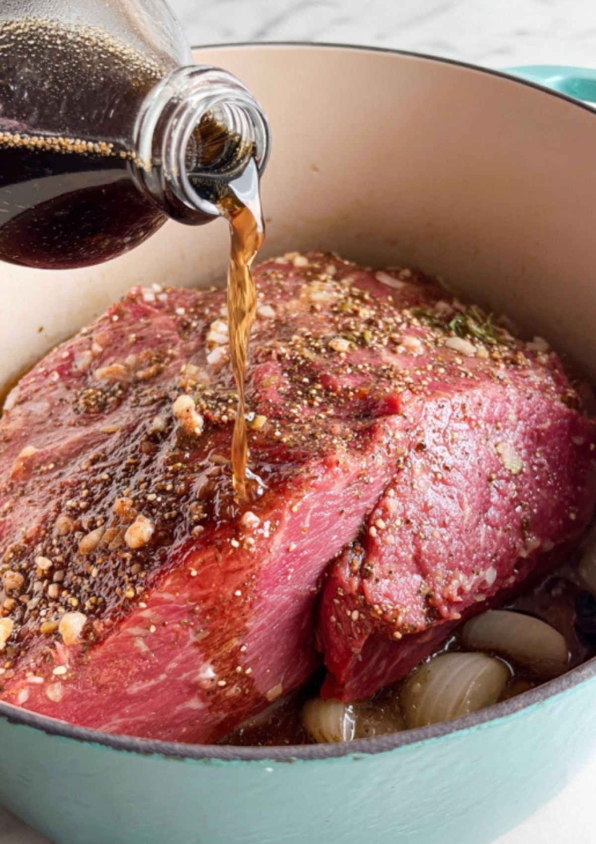 Beer being poured over corned beef brisket in a Dutch oven with onions and spices. This step adds rich, deep flavor to classic St. Patrick’s Day corned beef.