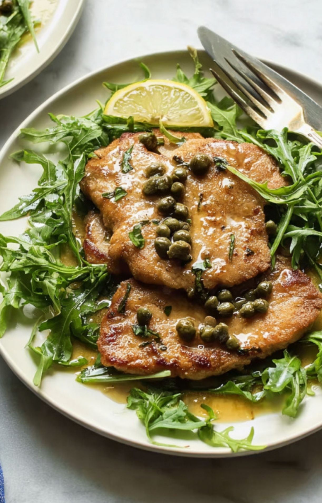 Plate of veal scallopini topped with tangy lemon caper sauce and herbs, great for weeknight dinners and entertaining.