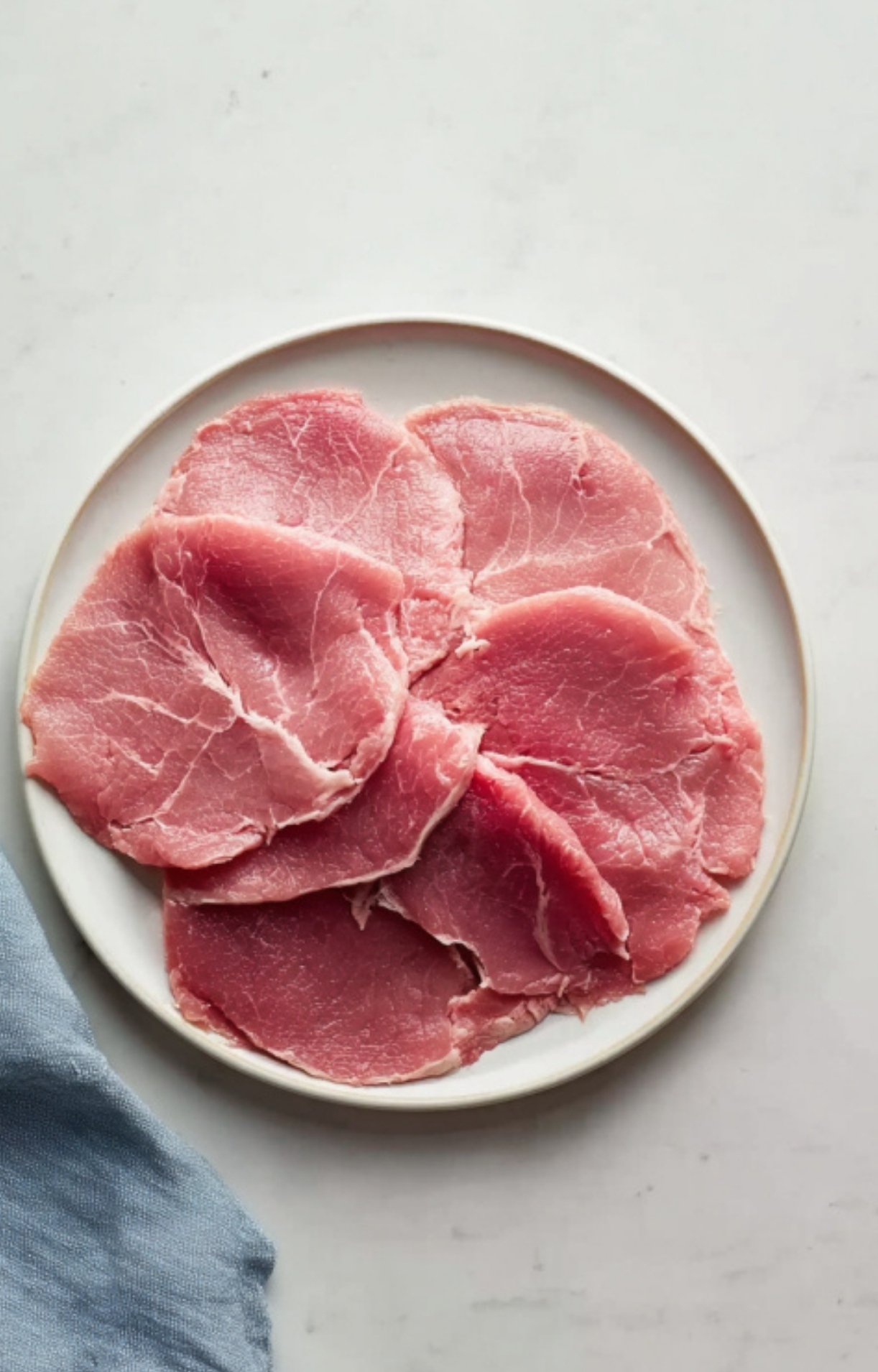 Plate of fresh veal scallopini cutlets ready to cook, perfect for light spring and summer recipes.