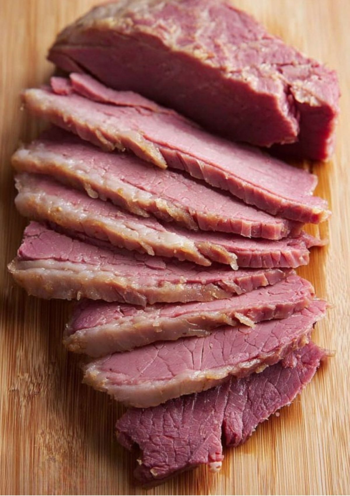 Juicy corned beef brisket sliced thinly across the grain on a wooden cutting board, ready for serving or sandwiches.