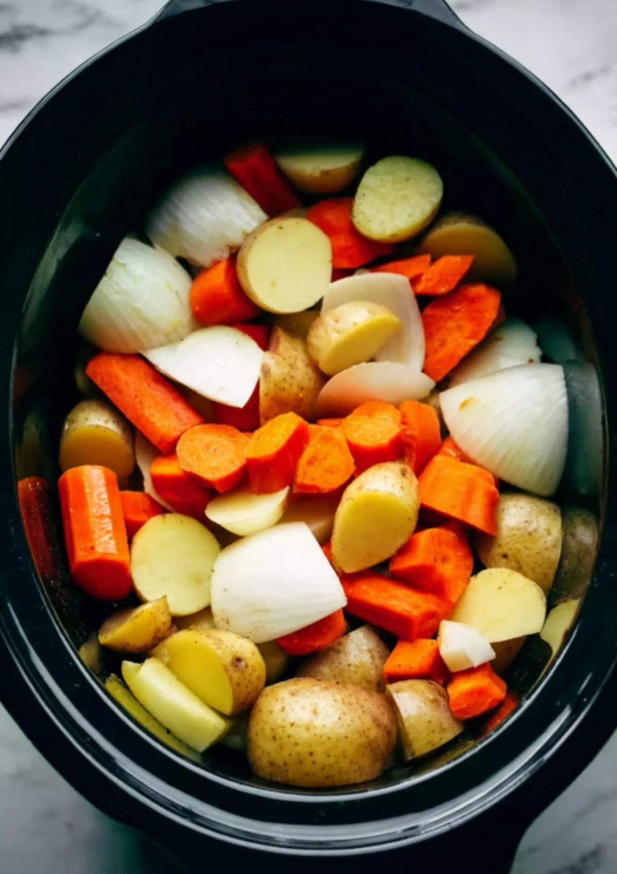 Chopped potatoes, carrots, and onions in a slow cooker, ready to cook with corned beef for a hearty Irish meal.