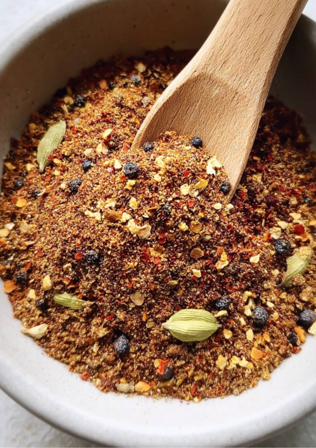 Homemade Corned Beef Spice Packet being scooped with a wooden spoon, highlighting a blend of red pepper flakes, cardamom pods, and black peppercorns.