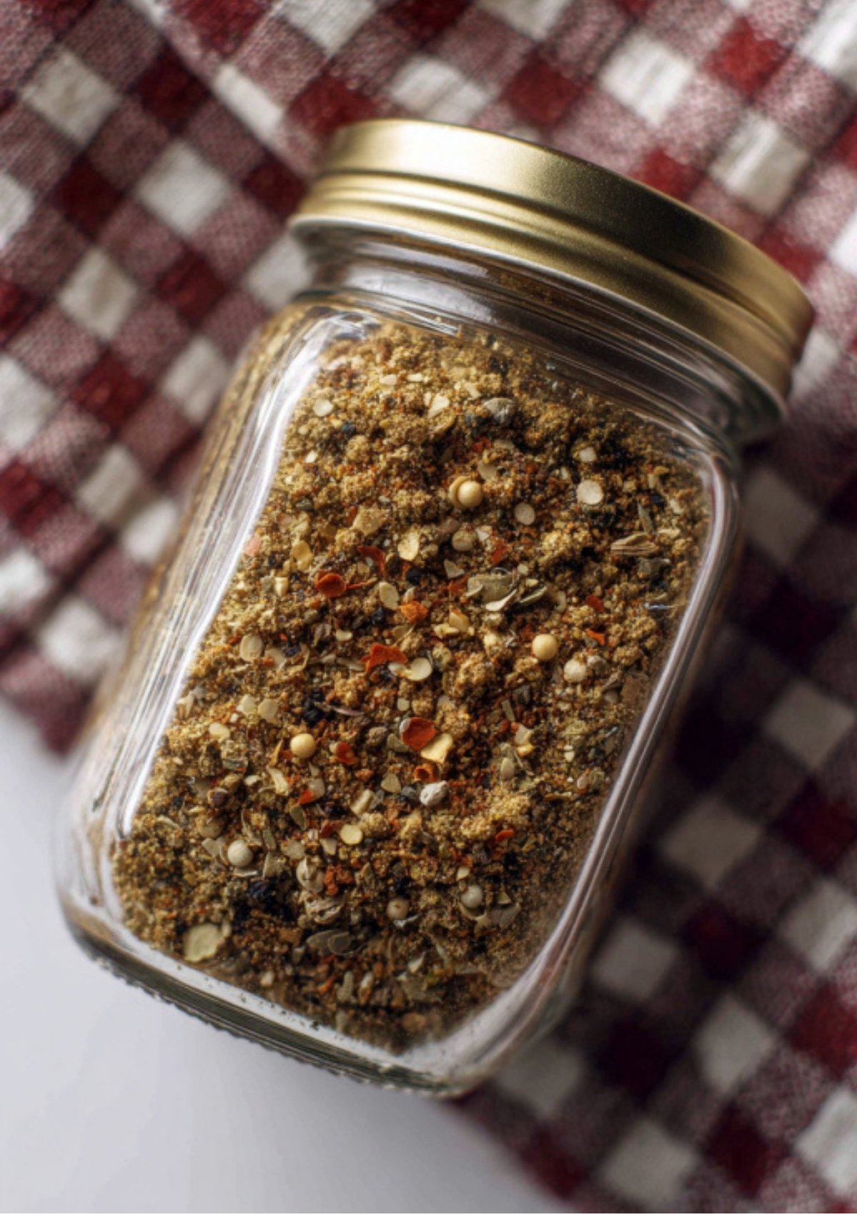 Glass jar filled with homemade Corned Beef Spice Packet, sitting on a checkered kitchen towel.