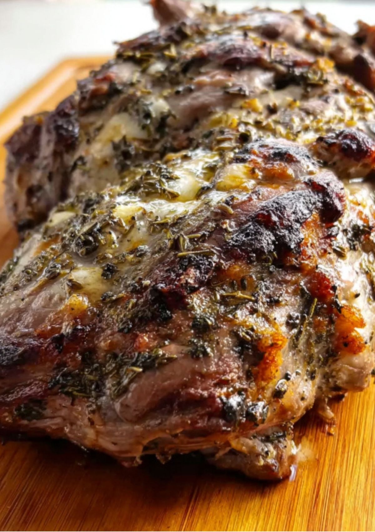 Raw leg of lamb surrounded by fresh rosemary, mint, olive oil, garlic, anchovies, and salt on a white table