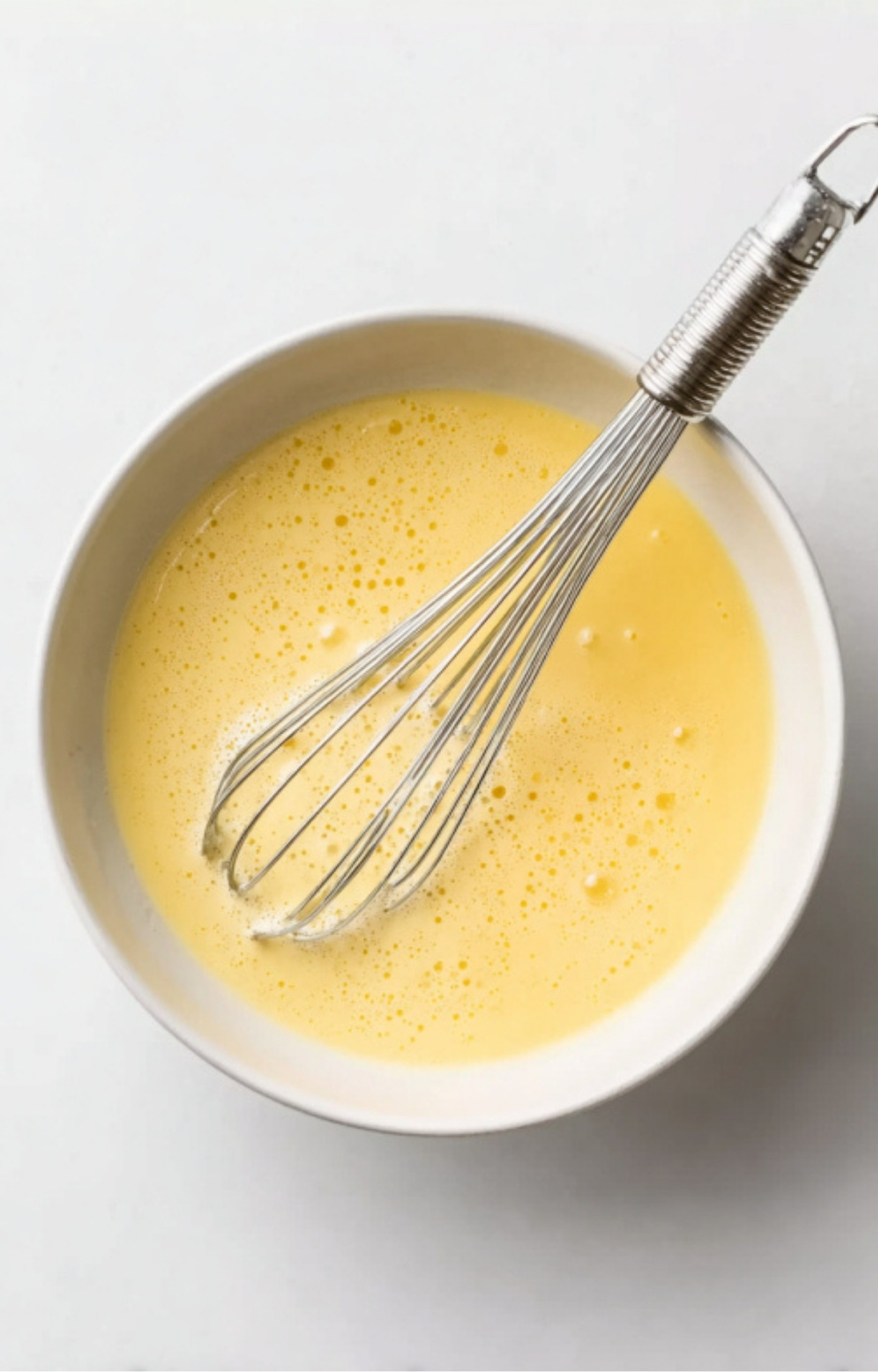 Bowl of lightly beaten egg mixture with a metal whisk, used for breading veal cutlets.