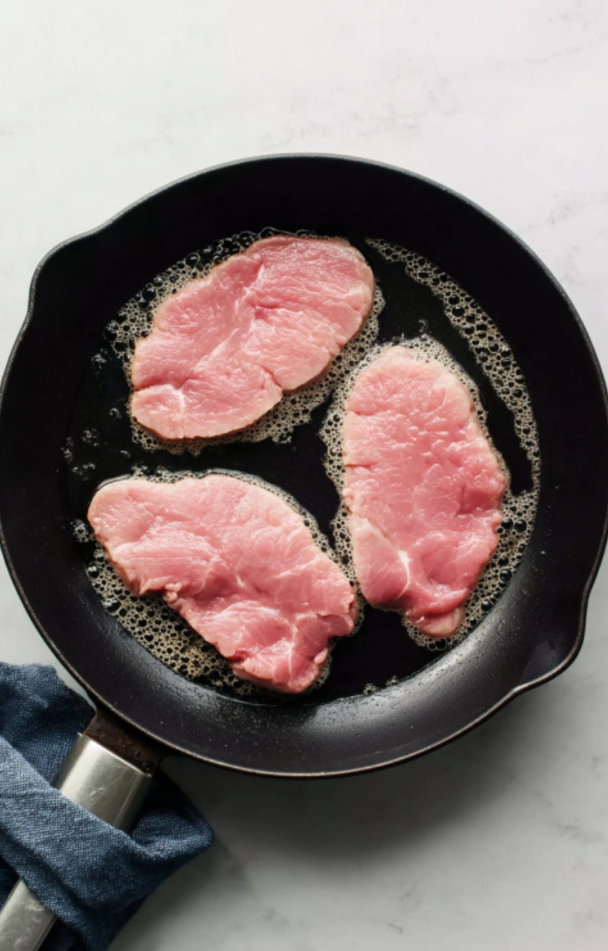 Raw veal scallopini cutlets sizzling in skillet, a simple step for making tender veal with lemon and capers.