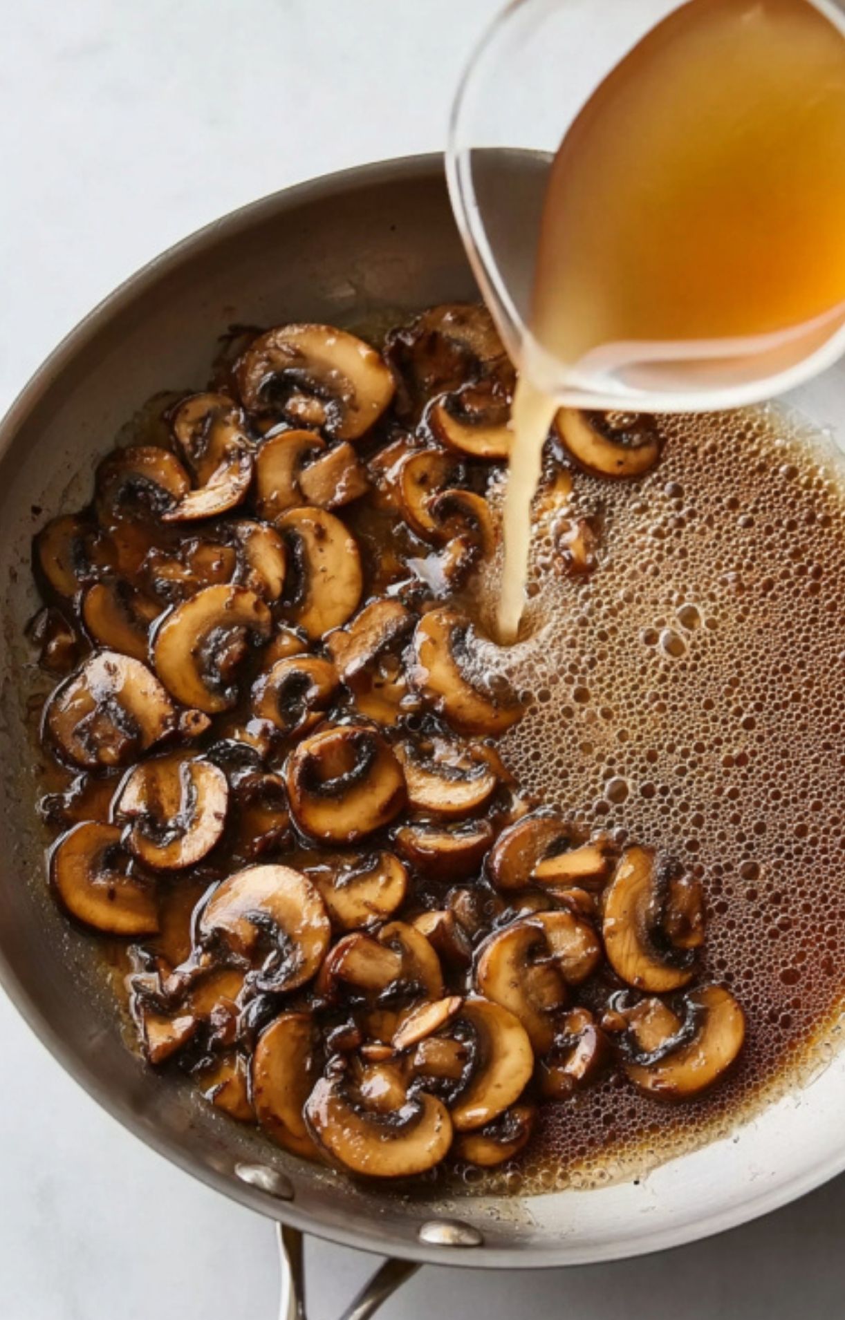 Pouring chicken broth into sautéed mushrooms in a skillet, step for making Marsala mushroom sauce