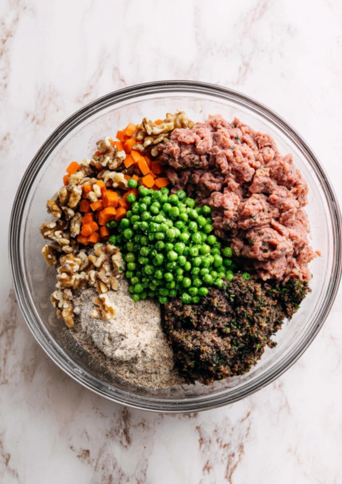 All the ingredients for vegan Wellington filling—ground vegan meat, peas, carrots, walnuts, and mushrooms—in a glass bowl. Great for plant-based Christmas and Thanksgiving recipes.