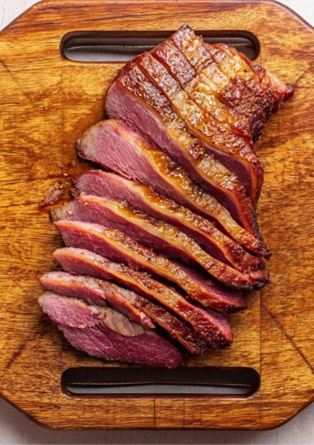 Slices of juicy corned beef brisket arranged neatly on a wooden cutting board, showing a tender, flavorful texture and a golden crust.