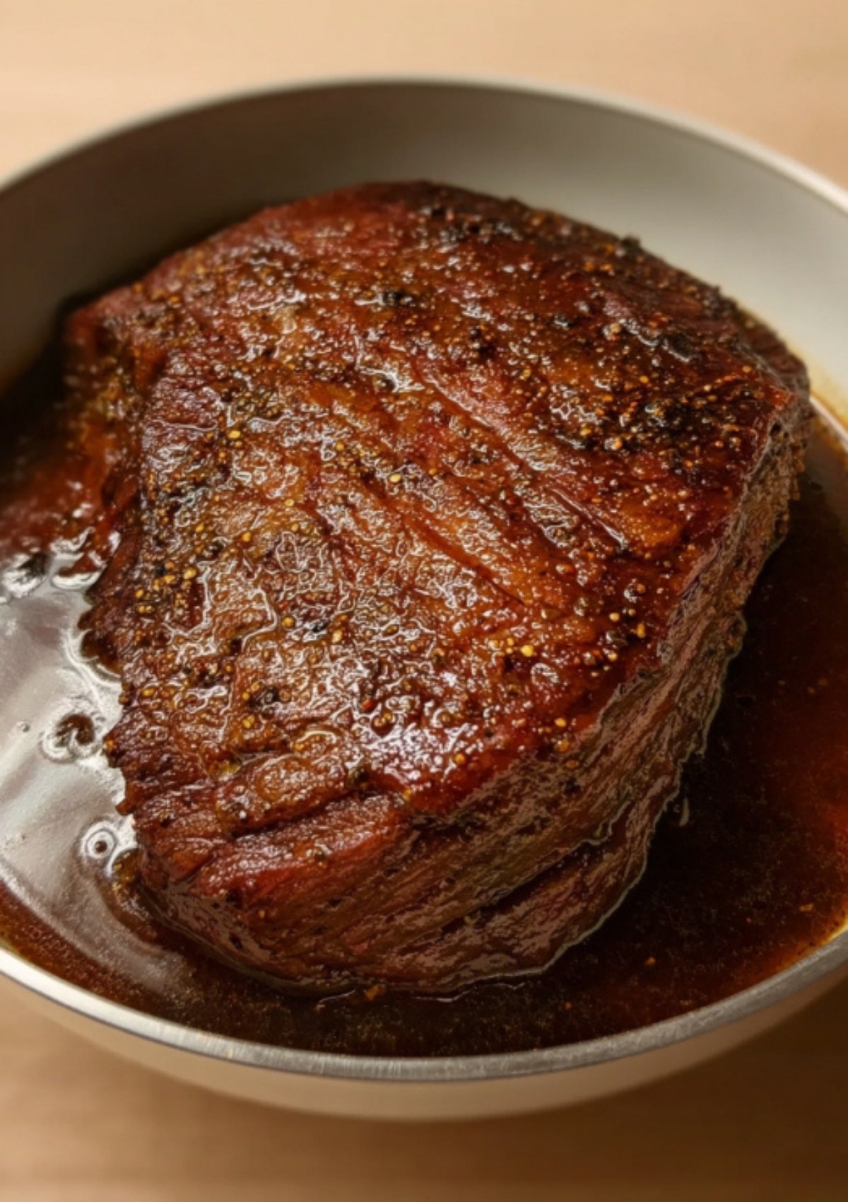 Corned beef brisket roasting in a pan filled with savory cooking liquid for extra juicy and tender meat.