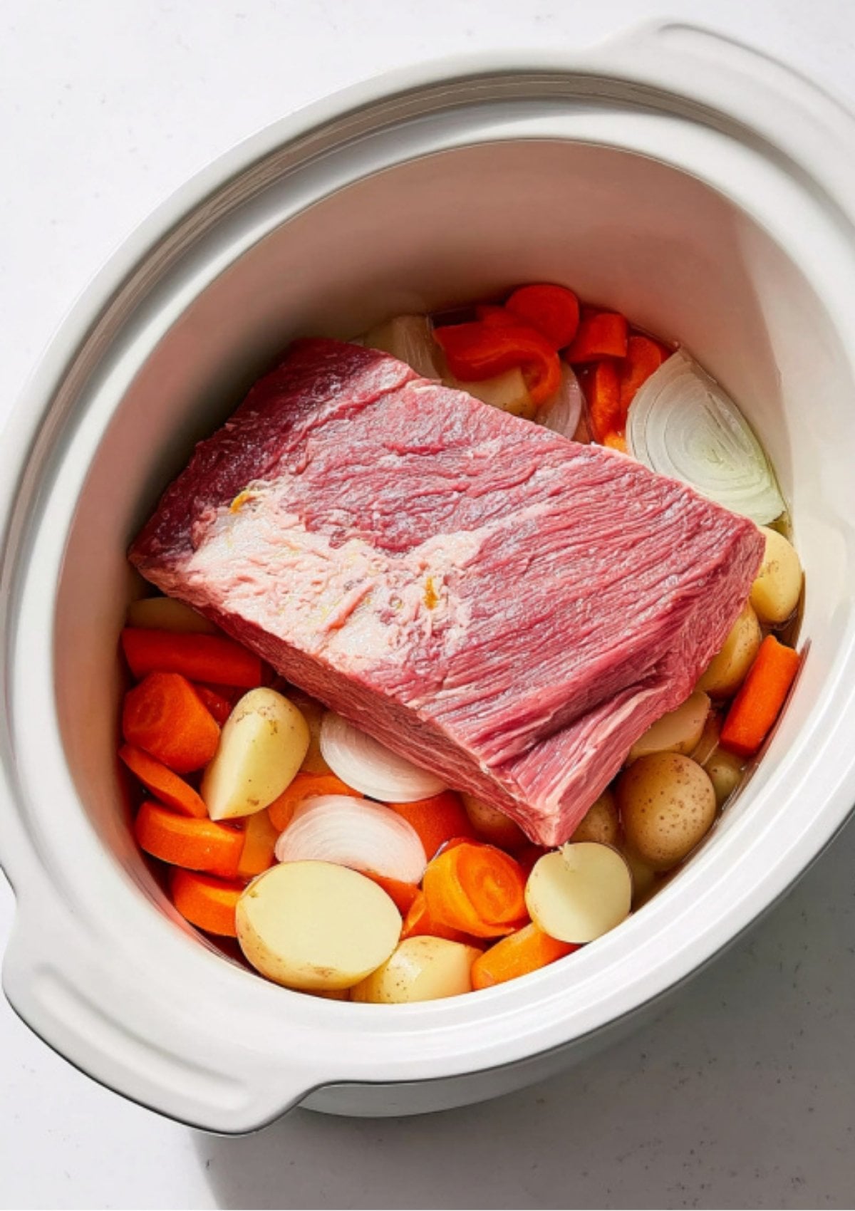 Uncooked corned beef brisket, potatoes, carrots, and onions arranged in an Instant Pot, ready for pressure cooking. Simple prep for a hearty family meal.