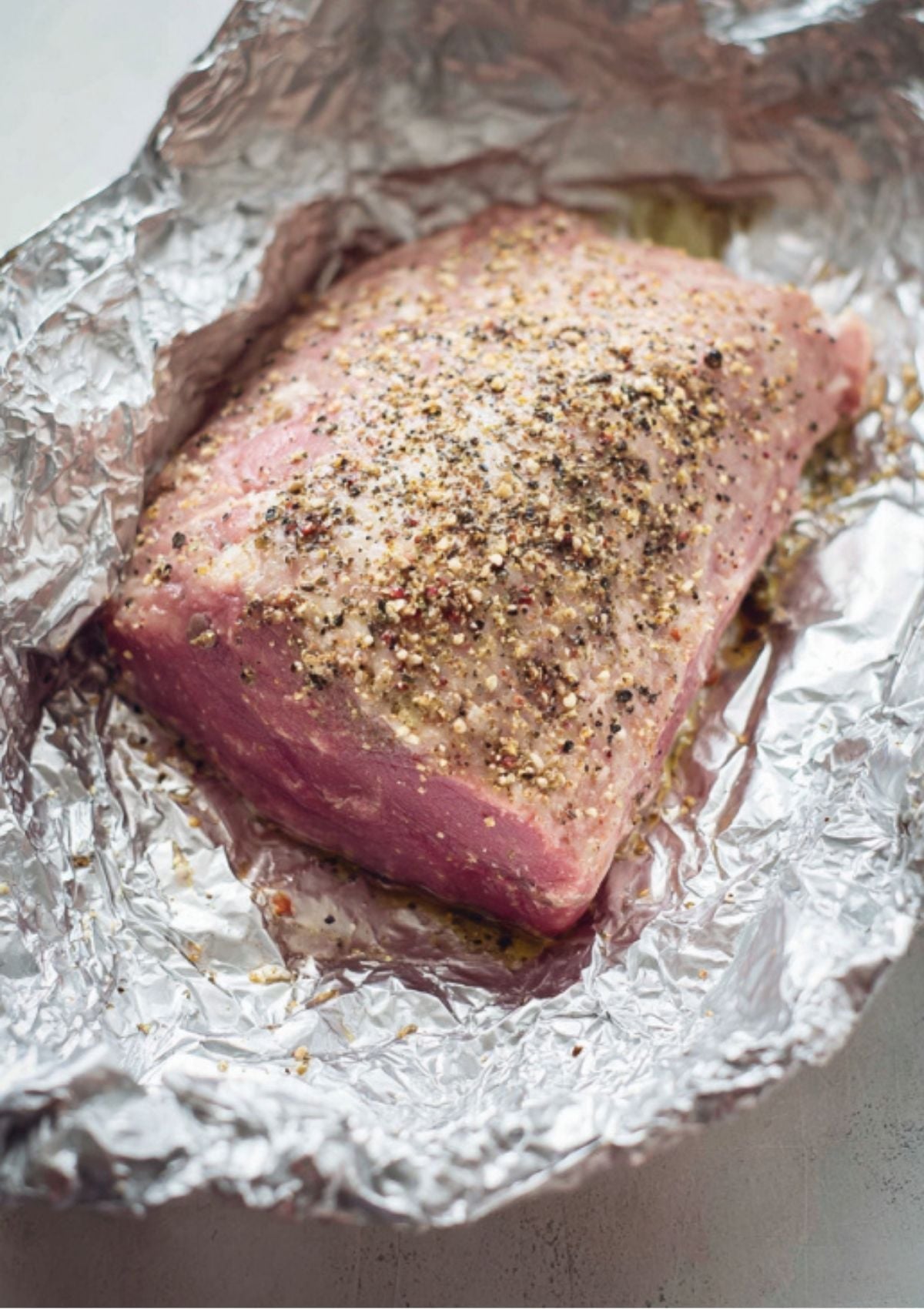 Uncooked corned beef brisket covered with spices and pepper, resting on foil before baking. Easy prep for the juiciest oven baked corned beef.
