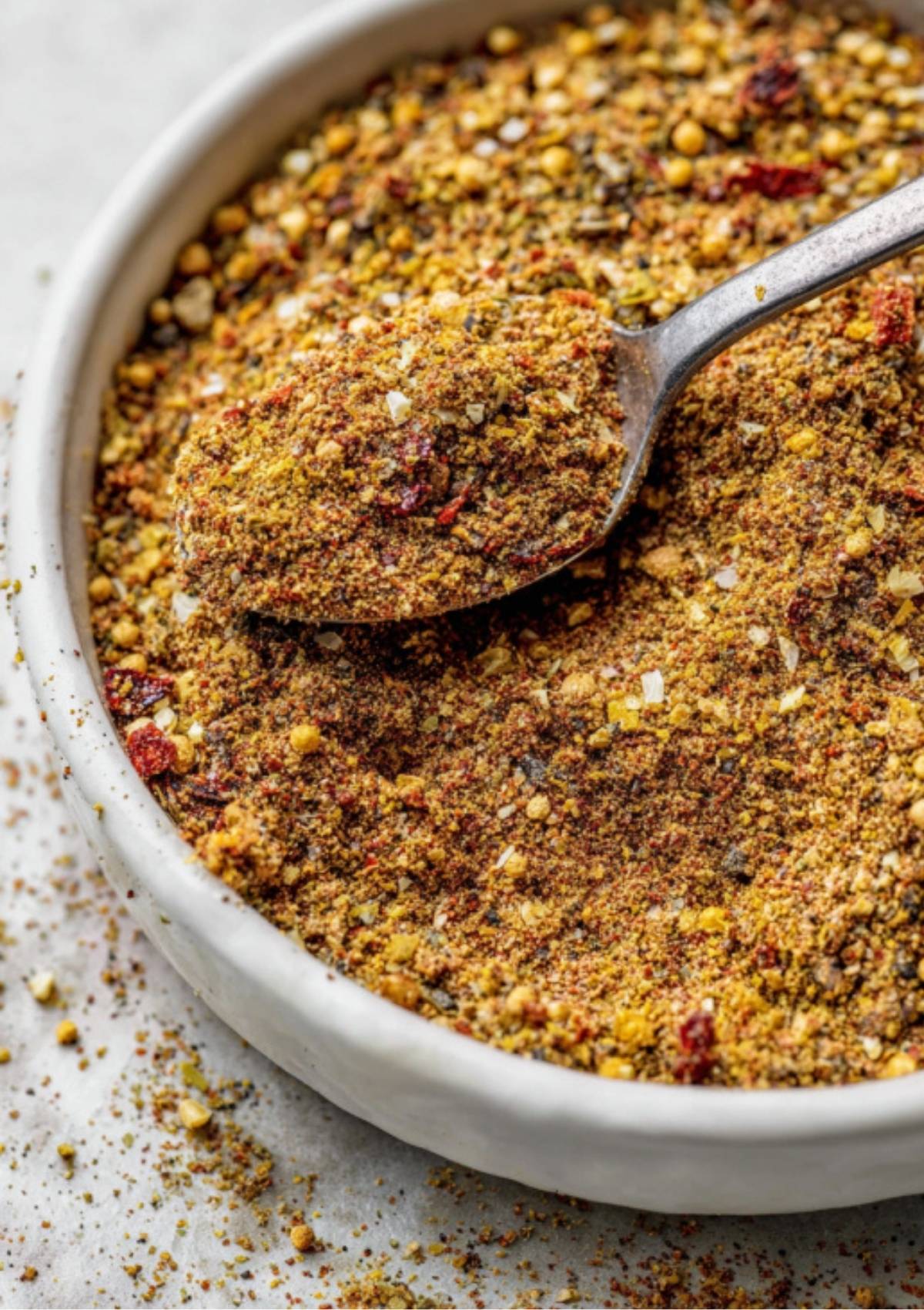 A small bowl filled with a coarse homemade corned beef spice blend, with a spoon scooping up the mixture.