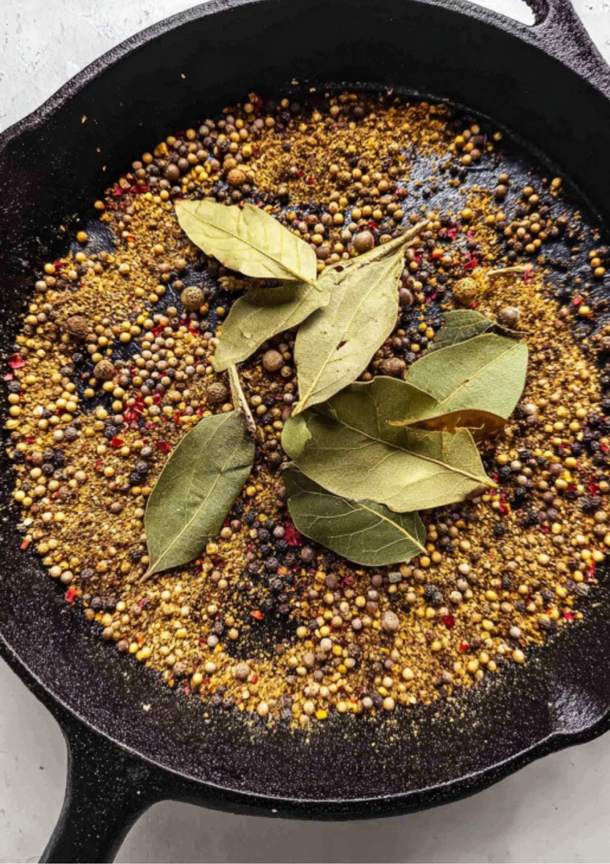 Spices and bay leaves in a cast iron pan after toasting, ready to grind for a flavorful Corned Beef Spice Packet.