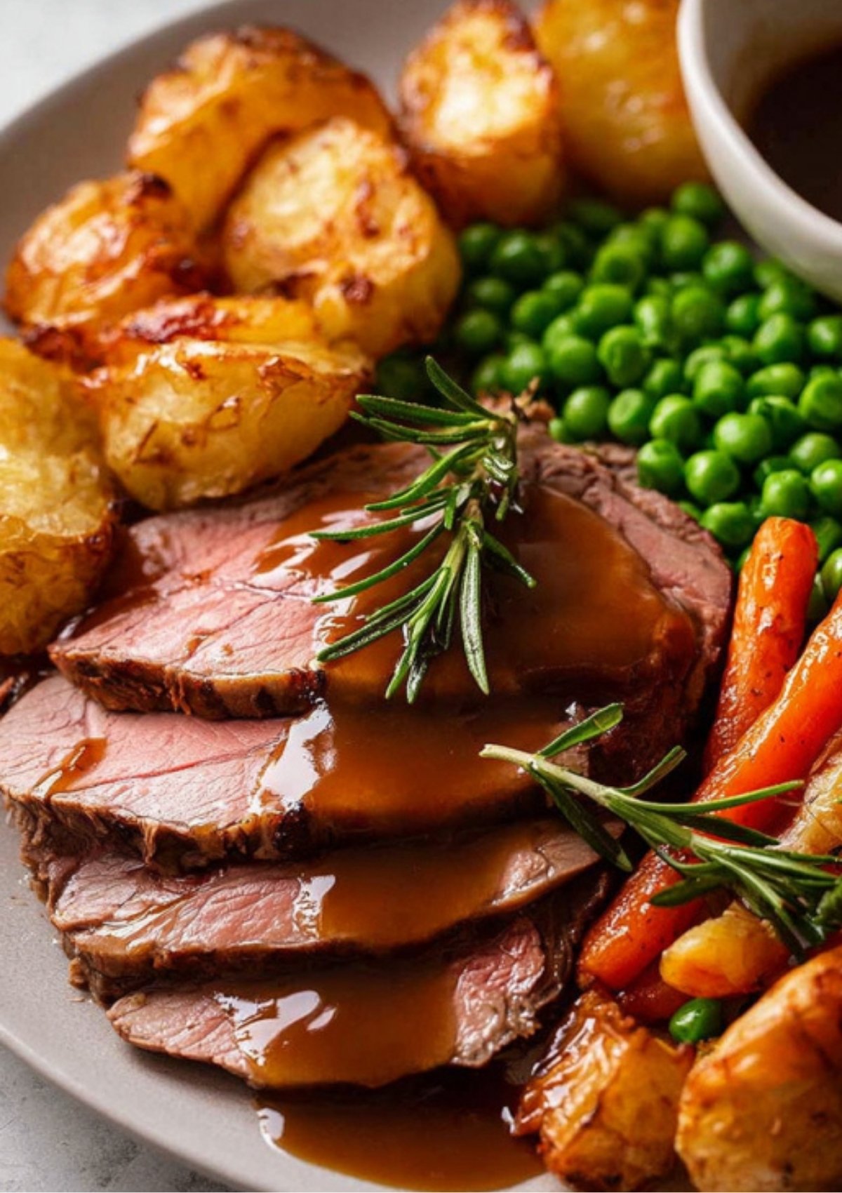 Sliced roast leg of lamb served with gravy, roast potatoes, peas, and carrots