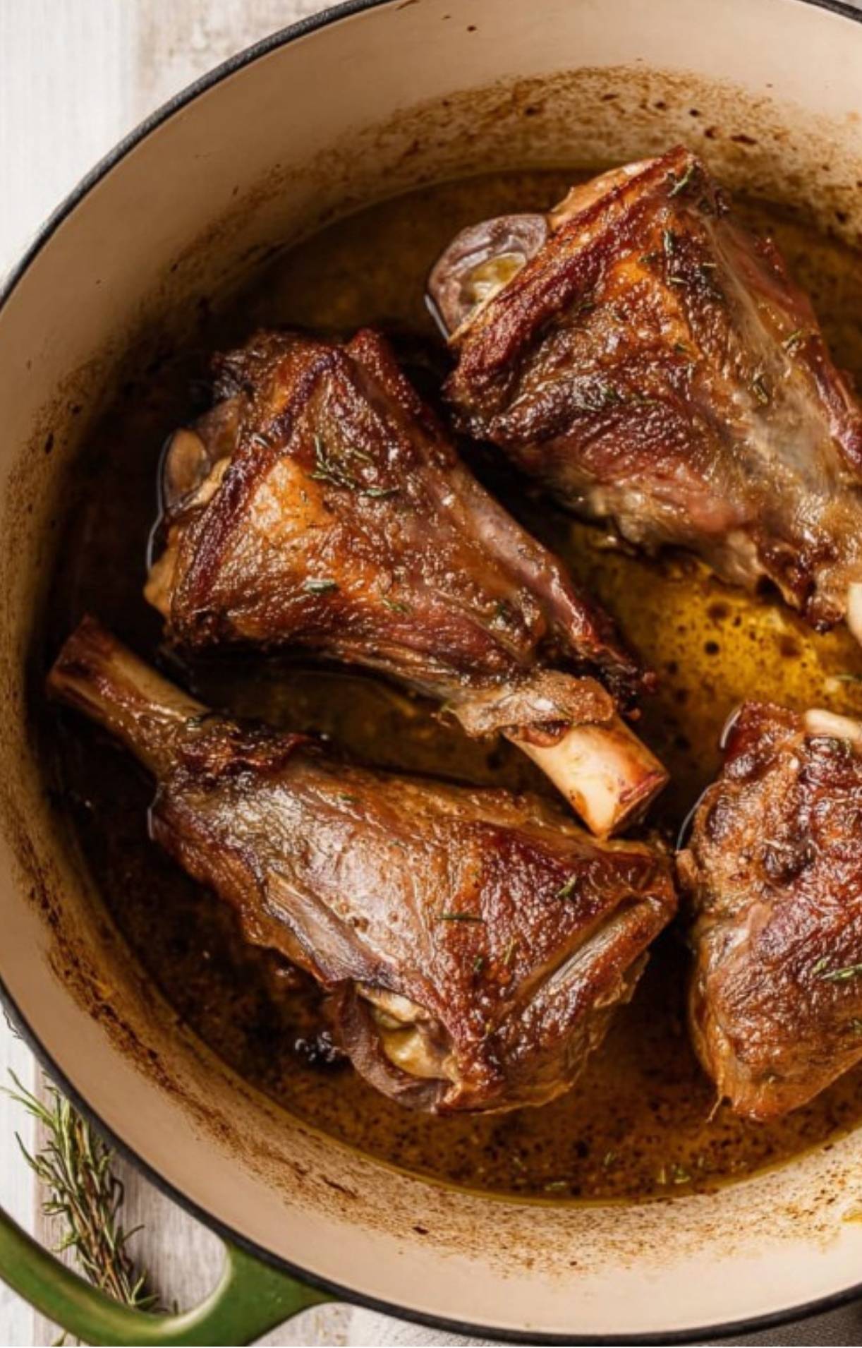 Four browned lamb shanks simmering in a Dutch oven with rich juices.