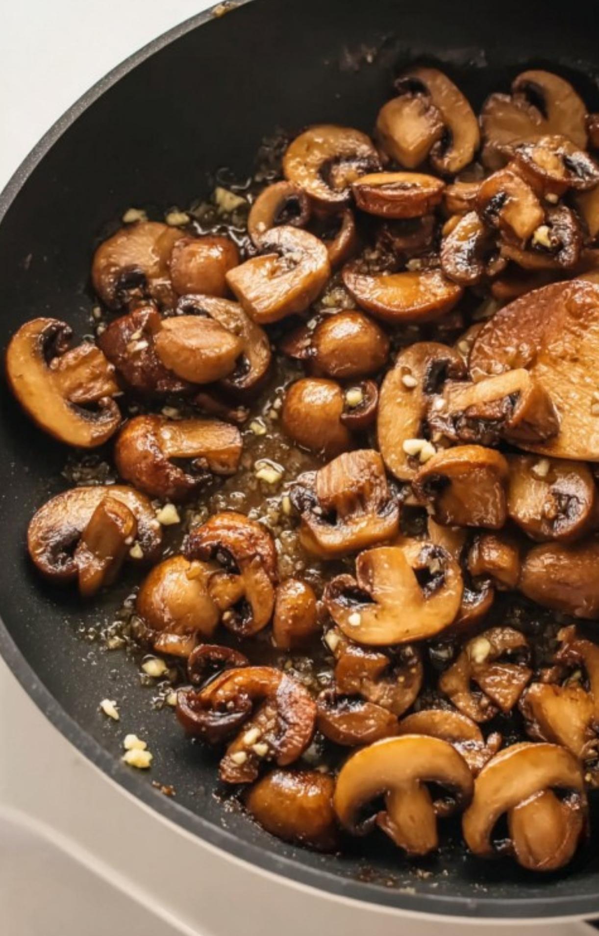Sliced mushrooms and garlic sizzling in a pan, ready to become a rich and creamy sauce for veal scallopini. Cozy and flavorful dinner idea.