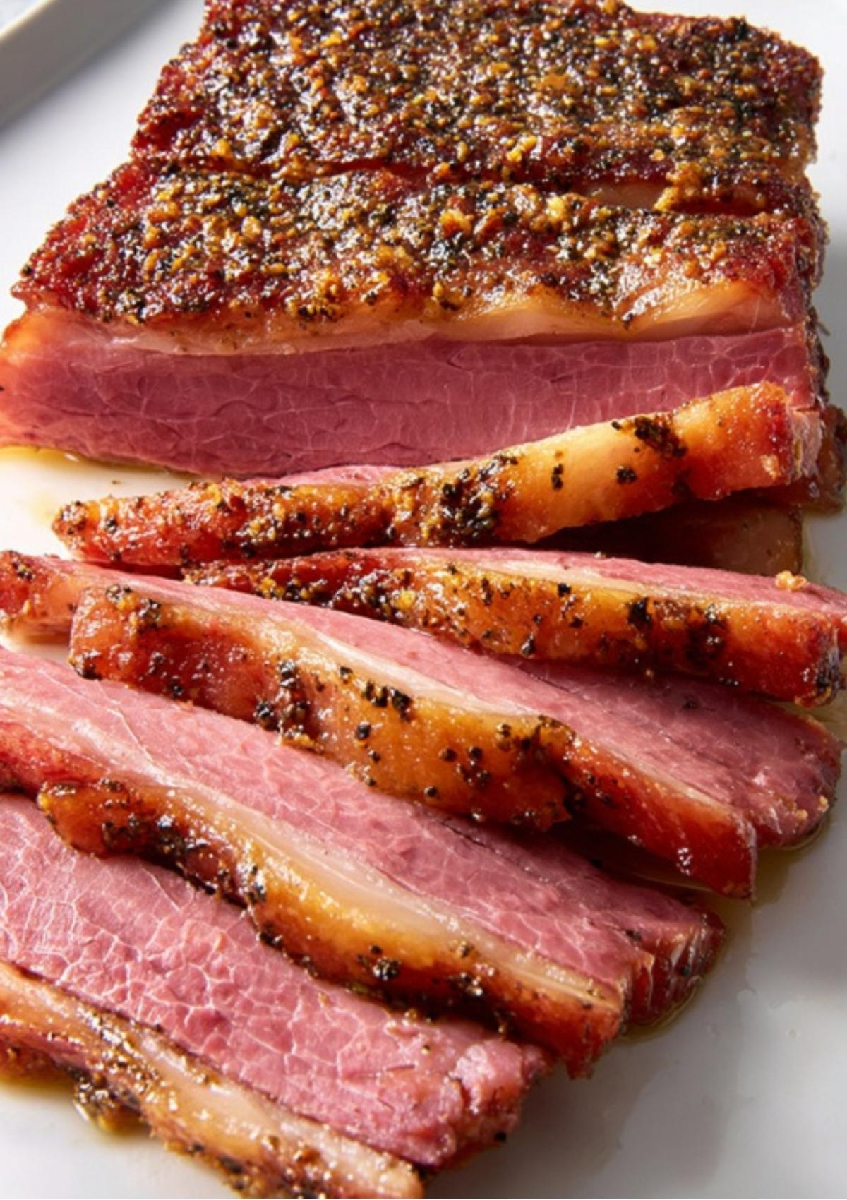 Thick slices of oven-roasted corned beef brisket with a golden brown spice crust on a white platter.