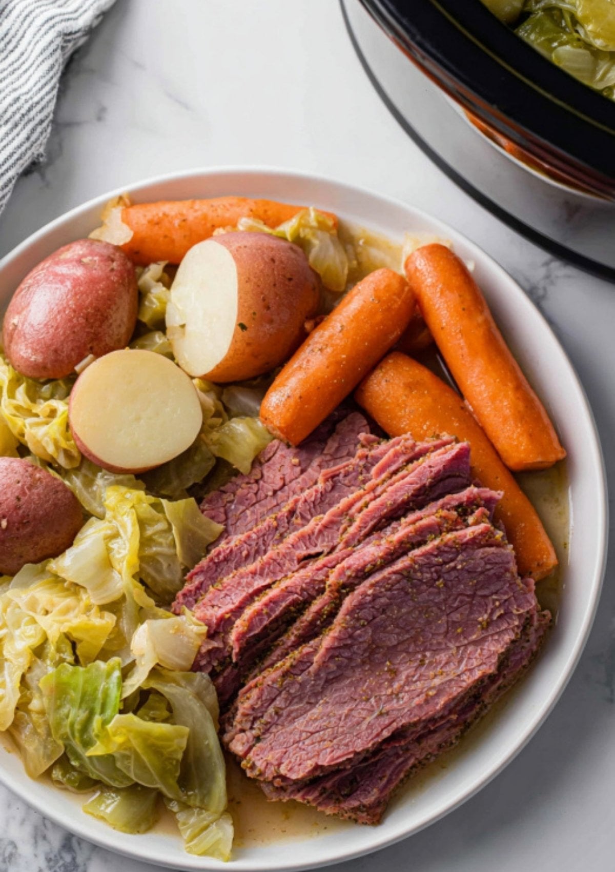 Plate with sliced corned beef, red potatoes, carrots, and cabbage. Comfort food classic, perfect for holiday meals, Sunday suppers, and easy slow cooker dinners.