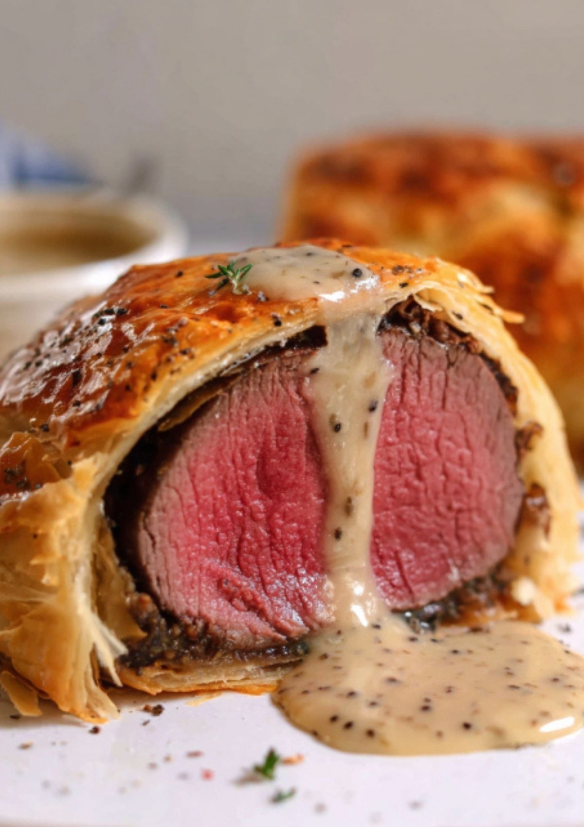 Golden baked Beef Wellington with creamy peppercorn sauce and a sprig of fresh thyme, perfect for Christmas, New Year’s, or special dinners.