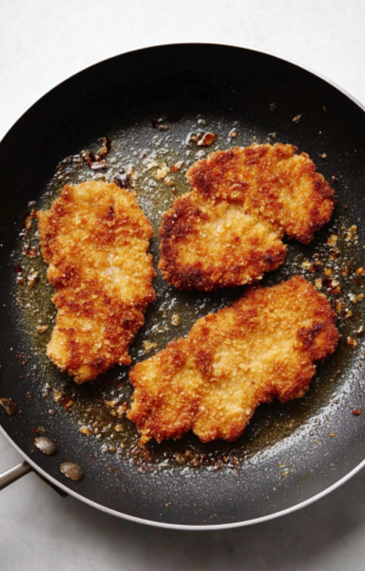 Veal scallopini cutlets sizzling in a pan for a crispy, golden Italian dinner.