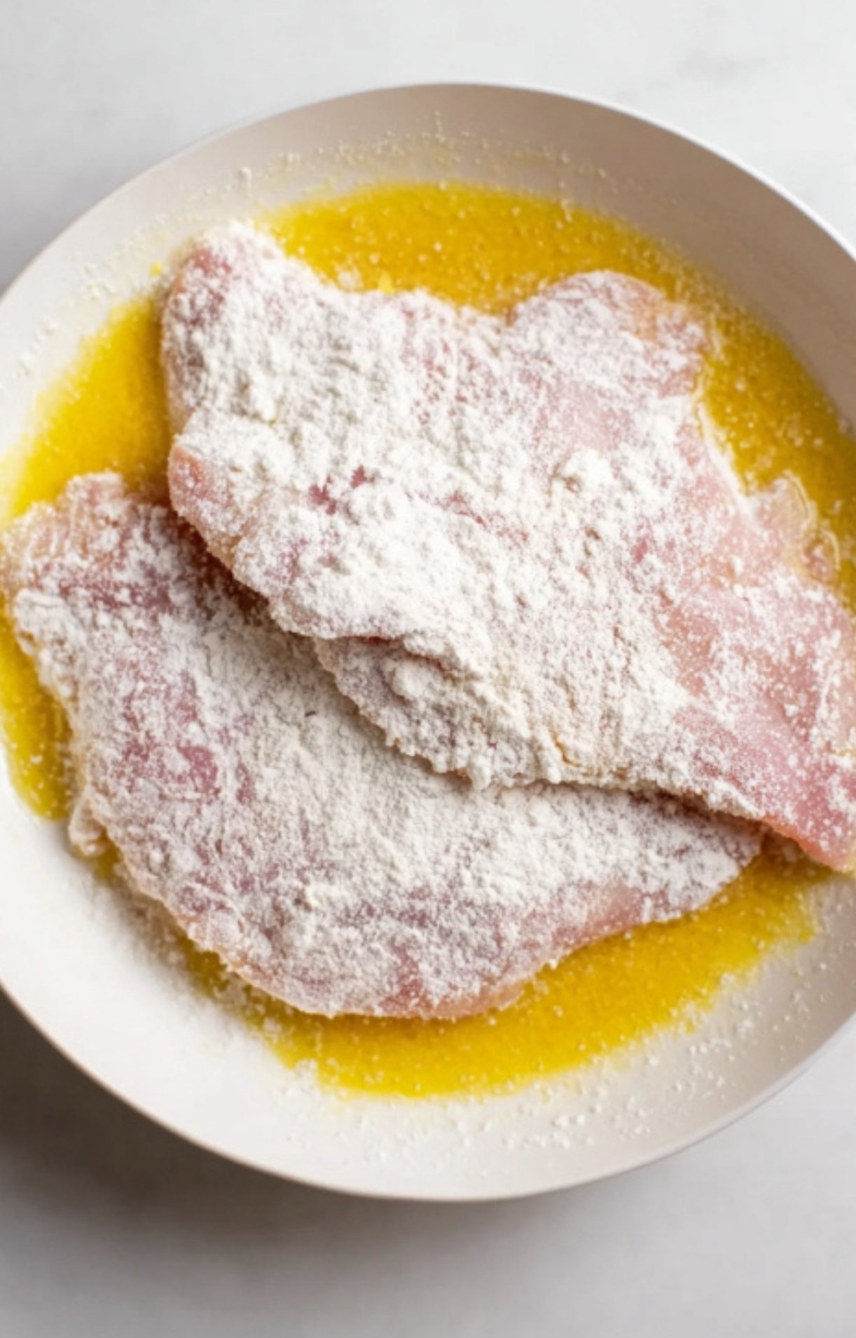 Raw veal cutlets coated in flour and egg, first step for crispy breaded veal Parmesan