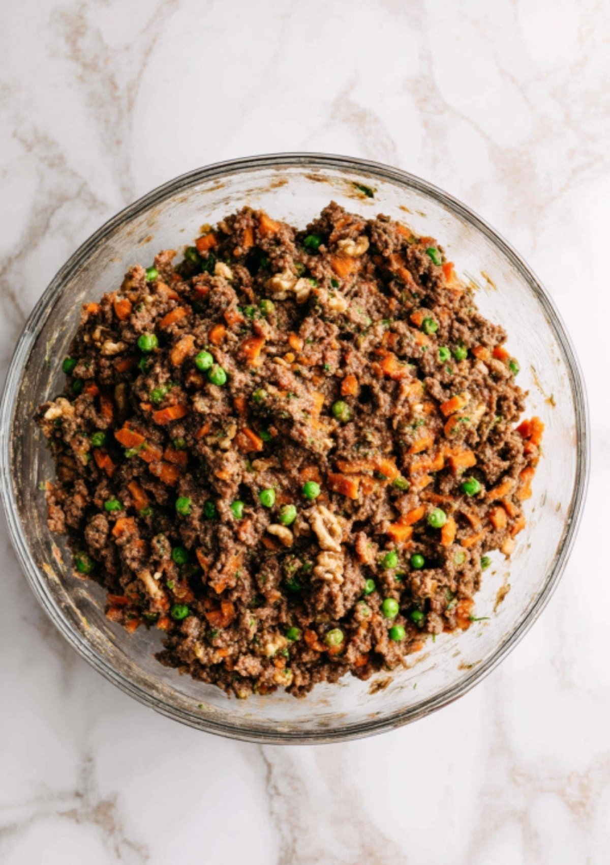 Mixing bowl with vegan Wellington filling featuring plant-based beef, mushrooms, peas, carrots, and walnuts. Ideal for preparing ahead for vegan holiday meals.