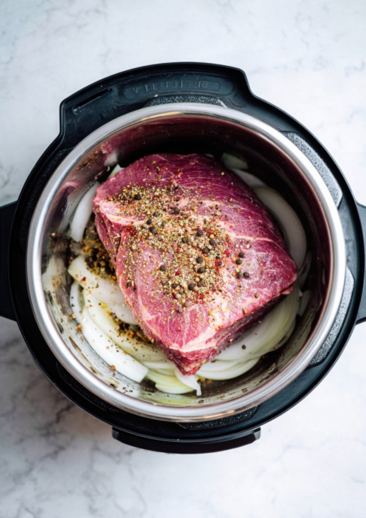Uncooked brisket topped with pickling spices on a bed of onions in an Instant Pot. Easy prep for classic pressure cooker corned beef, ready in a fraction of the time.