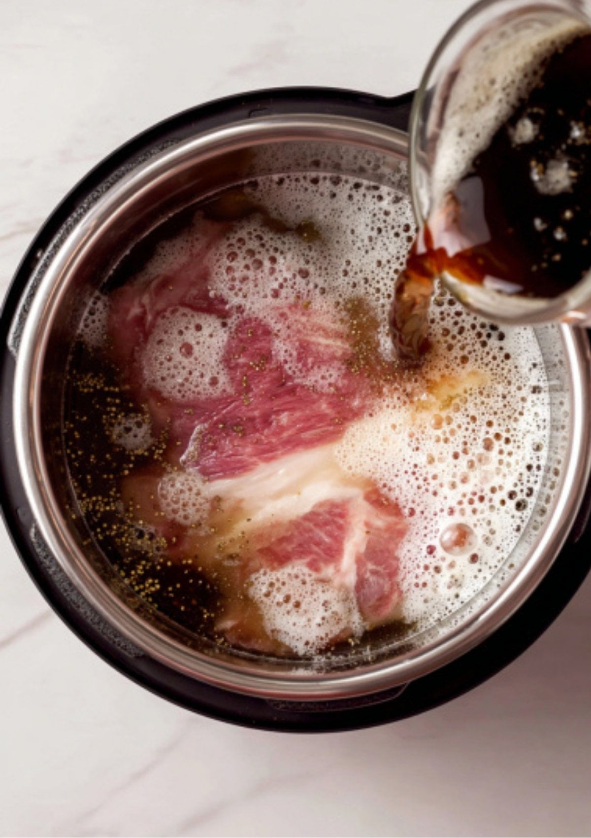 A dark stout beer being poured over raw beef brisket and pickling spices inside a pressure cooker to prepare Instant Pot Corned Beef.