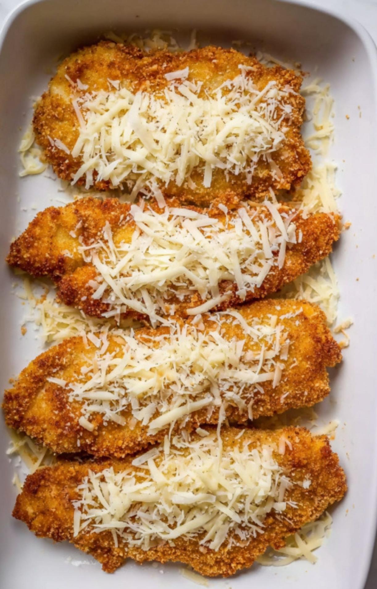Unbaked veal cutlets covered with shredded Parmesan and mozzarella cheese in a white baking dish