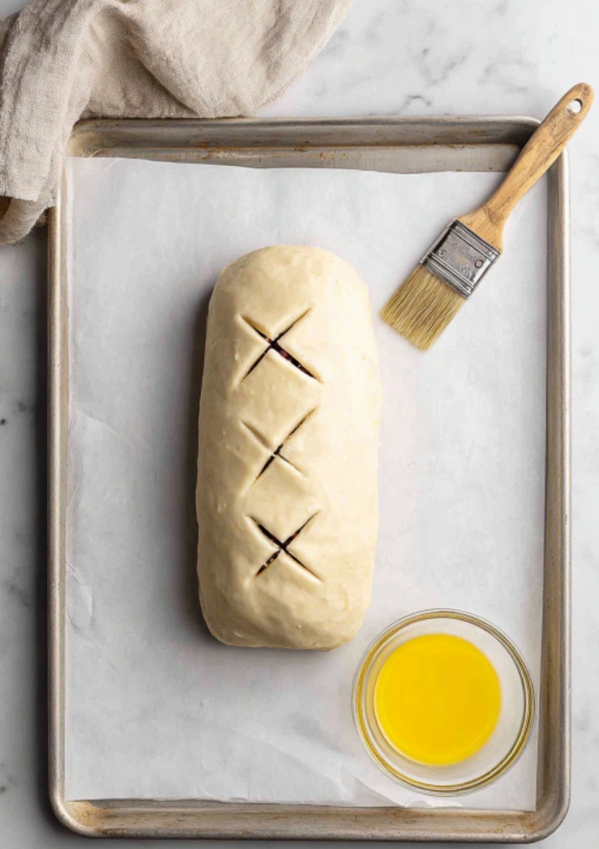 A plant-based Wellington wrapped in flaky pastry, scored and brushed with vegan butter, sitting on a baking tray before baking. Perfect for Christmas or Thanksgiving main dish.