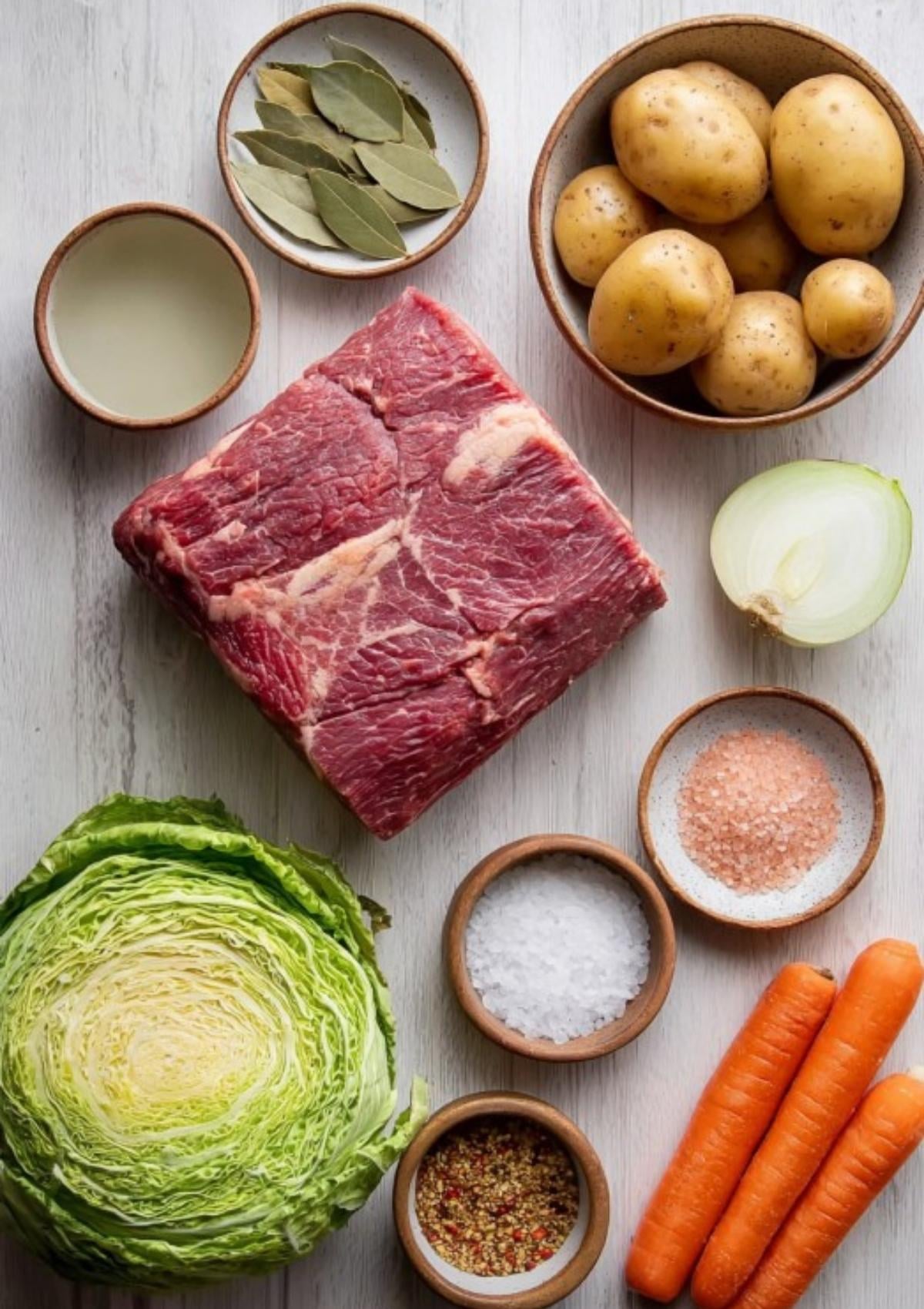 Raw brisket, cabbage, potatoes, carrots, and seasonings arranged for making homemade corned beef and cabbage.