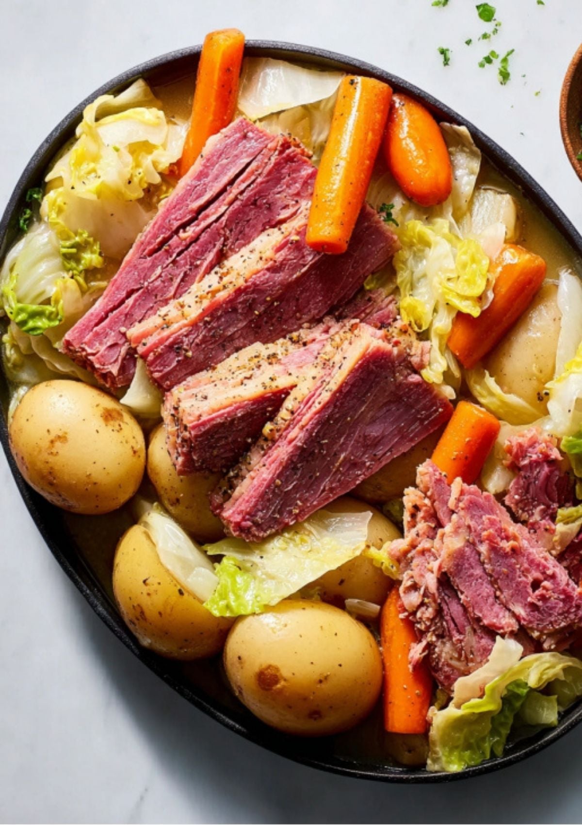 Cooked slices of corned beef with cabbage, carrots, and potatoes in a black dish. Classic Irish comfort food made fast in the pressure cooker.