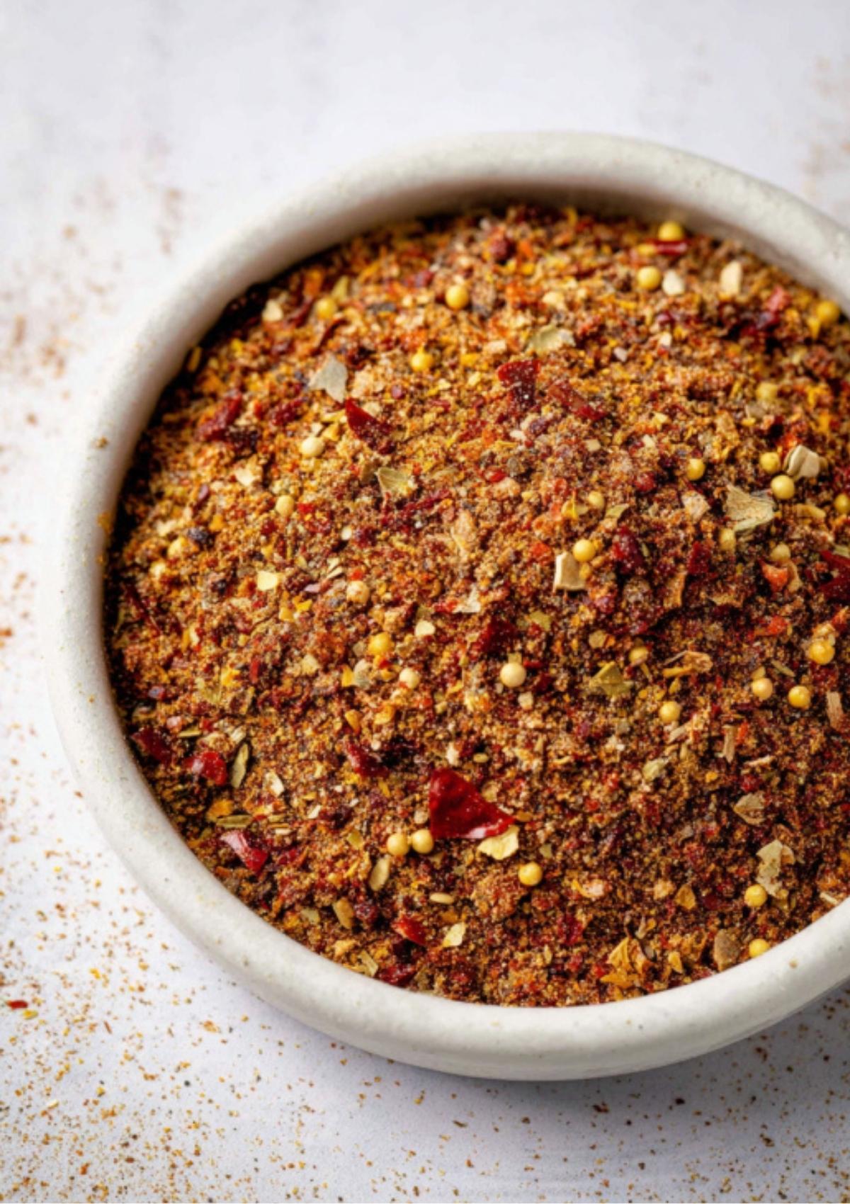 Overhead close-up of a bowl with red and yellow flecks of homemade corned beef seasoning blend.