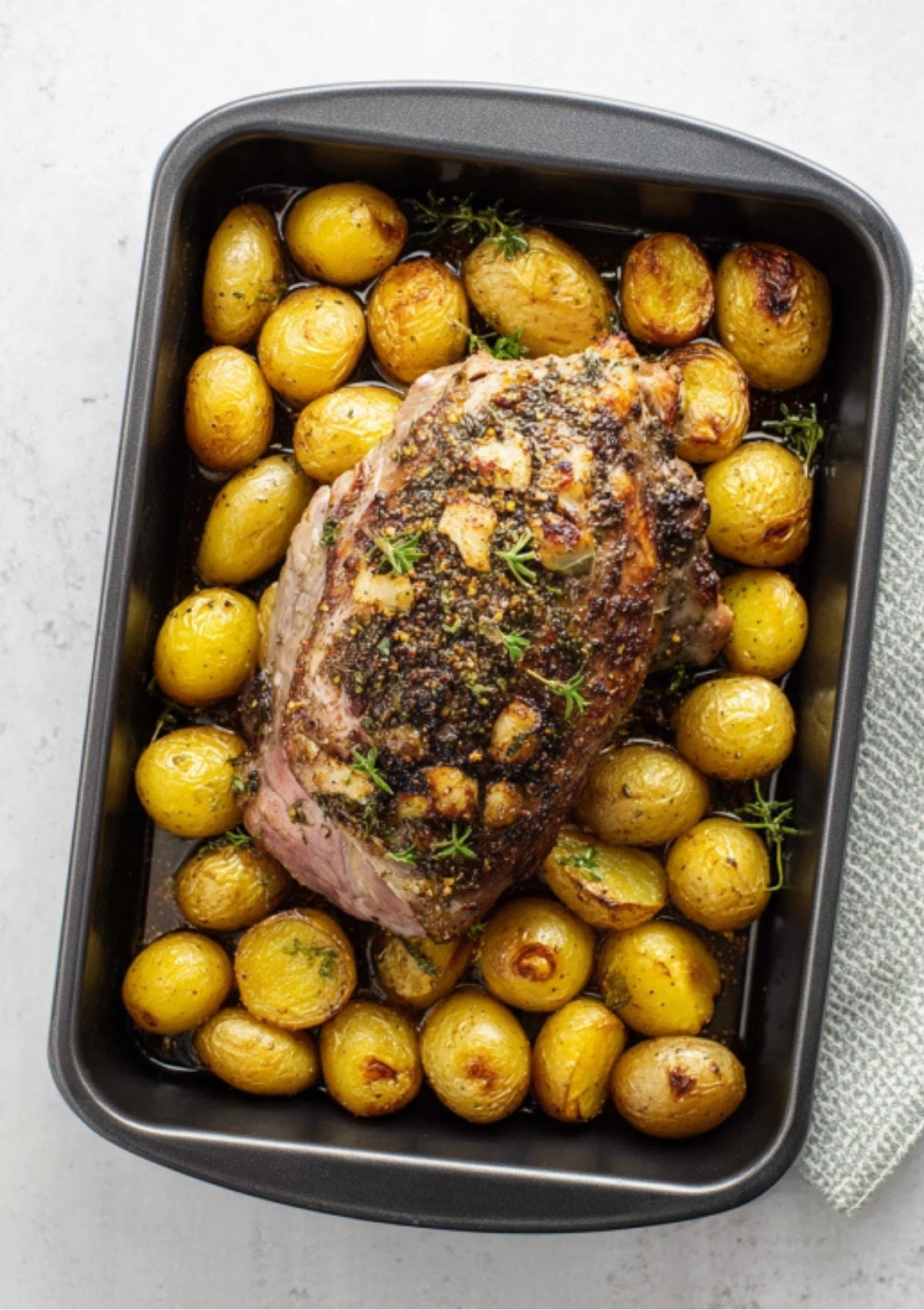 Juicy boneless leg of lamb roast surrounded by golden roasted potatoes in a black roasting pan