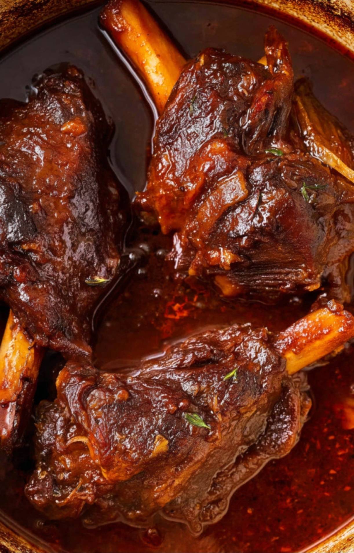 Lamb shanks braising in a deep, dark red wine sauce after hours of slow cooking.