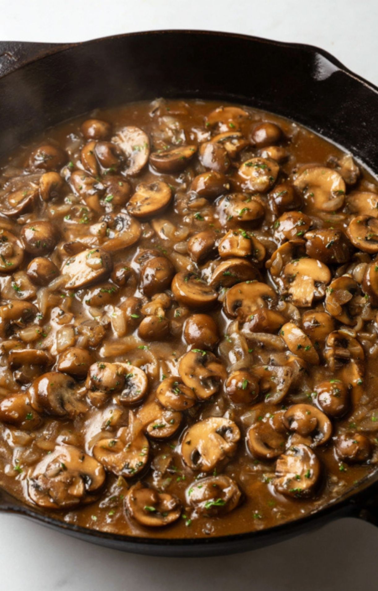 Sliced mushrooms and onions cooking in a rich brown sauce in a cast iron skillet.