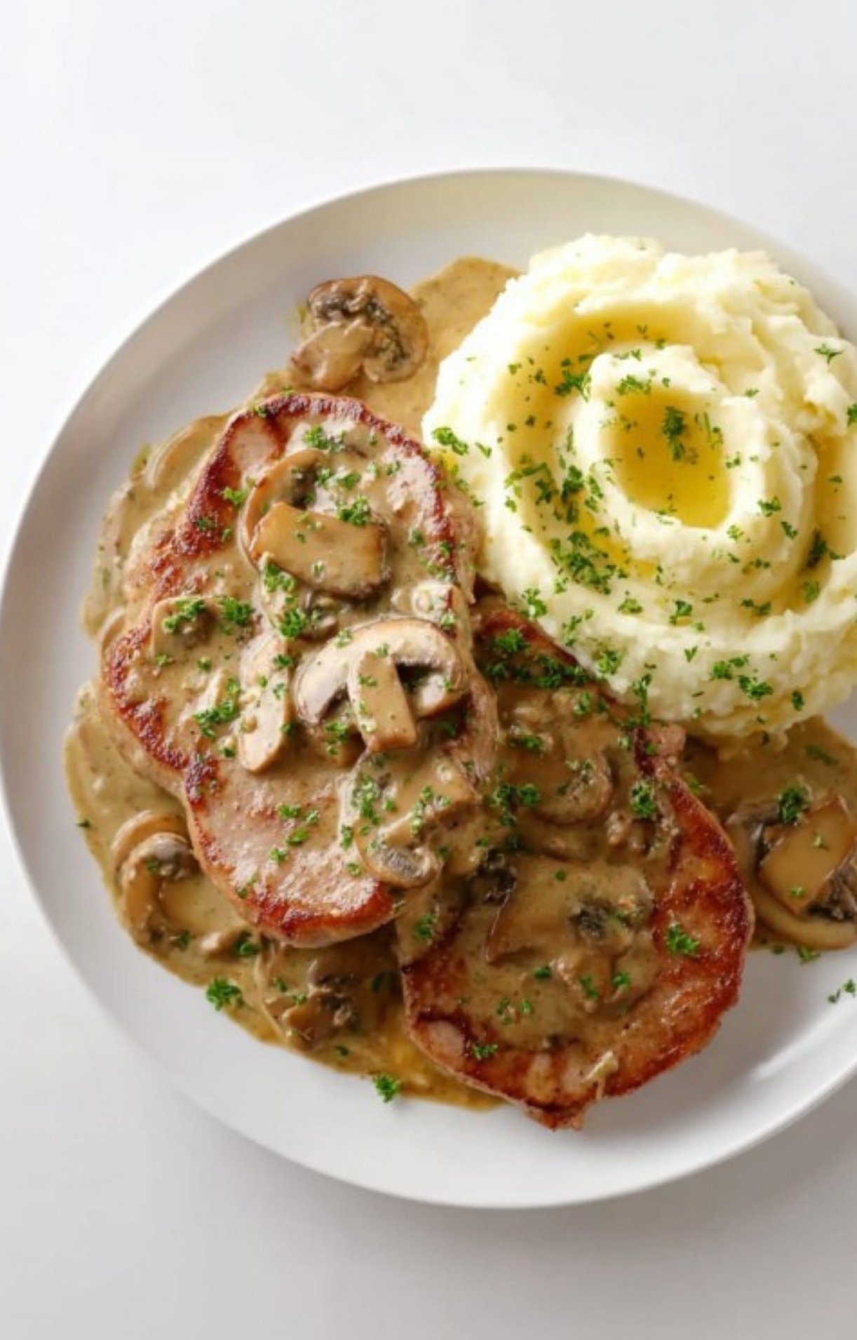 Plate of veal scallopini topped with creamy mushroom sauce, served alongside mashed potatoes. Ultimate comfort food for holidays or Sunday dinner.