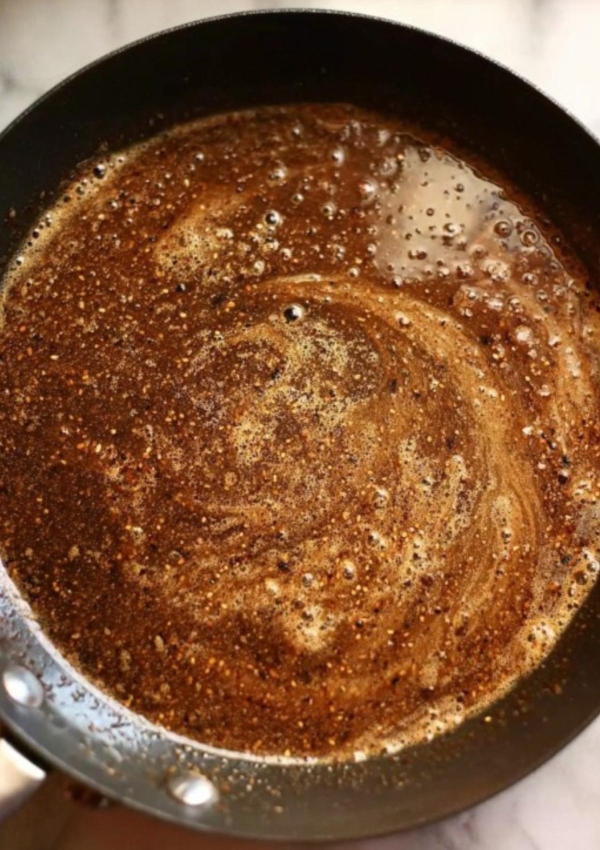 Peppercorn sauce swirling in a pan, rich brown color and visible black pepper, ready to serve with festive holiday beef dishes or Wellington.