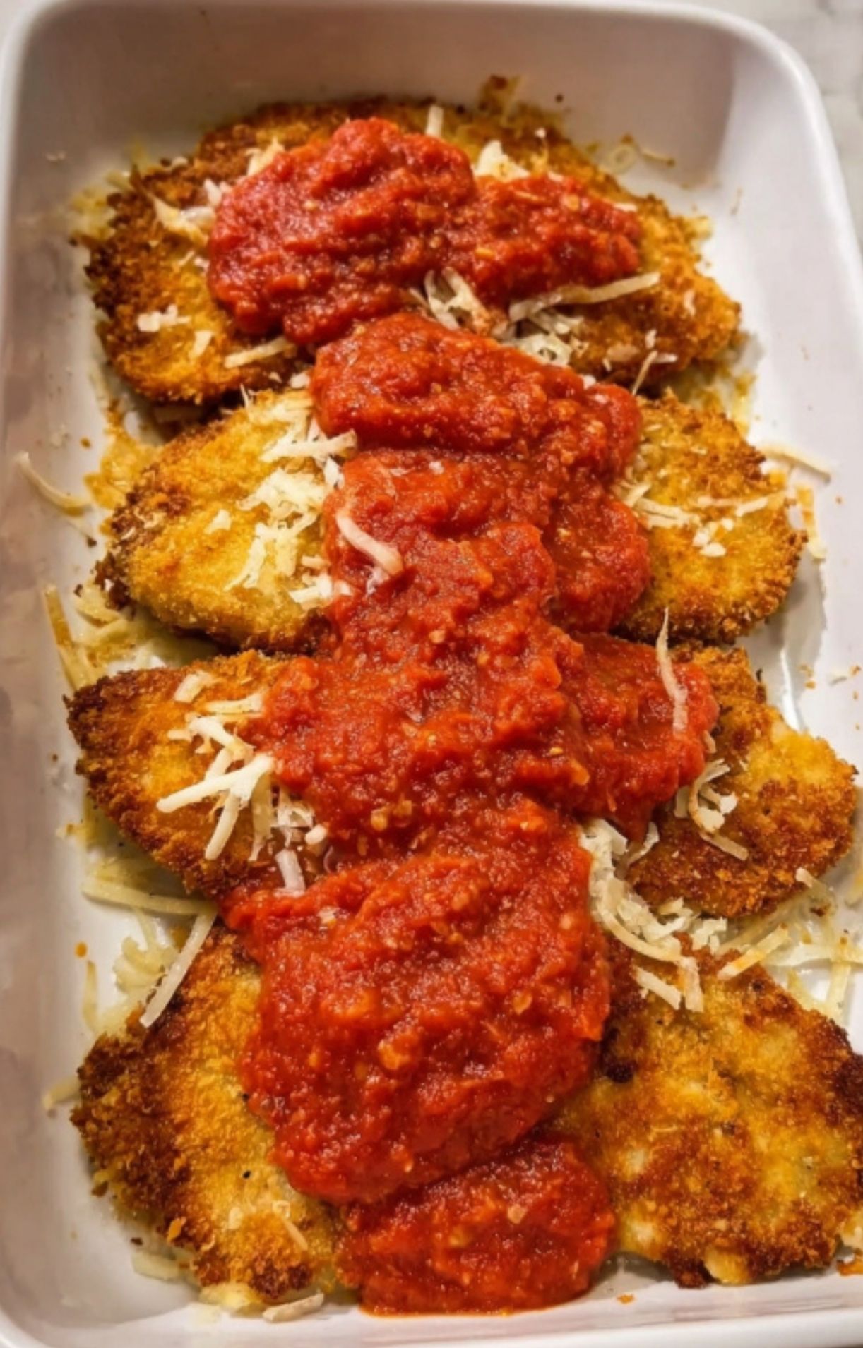 Breaded veal cutlets layered with tomato sauce in a dish, step before adding cheese for Parmesan