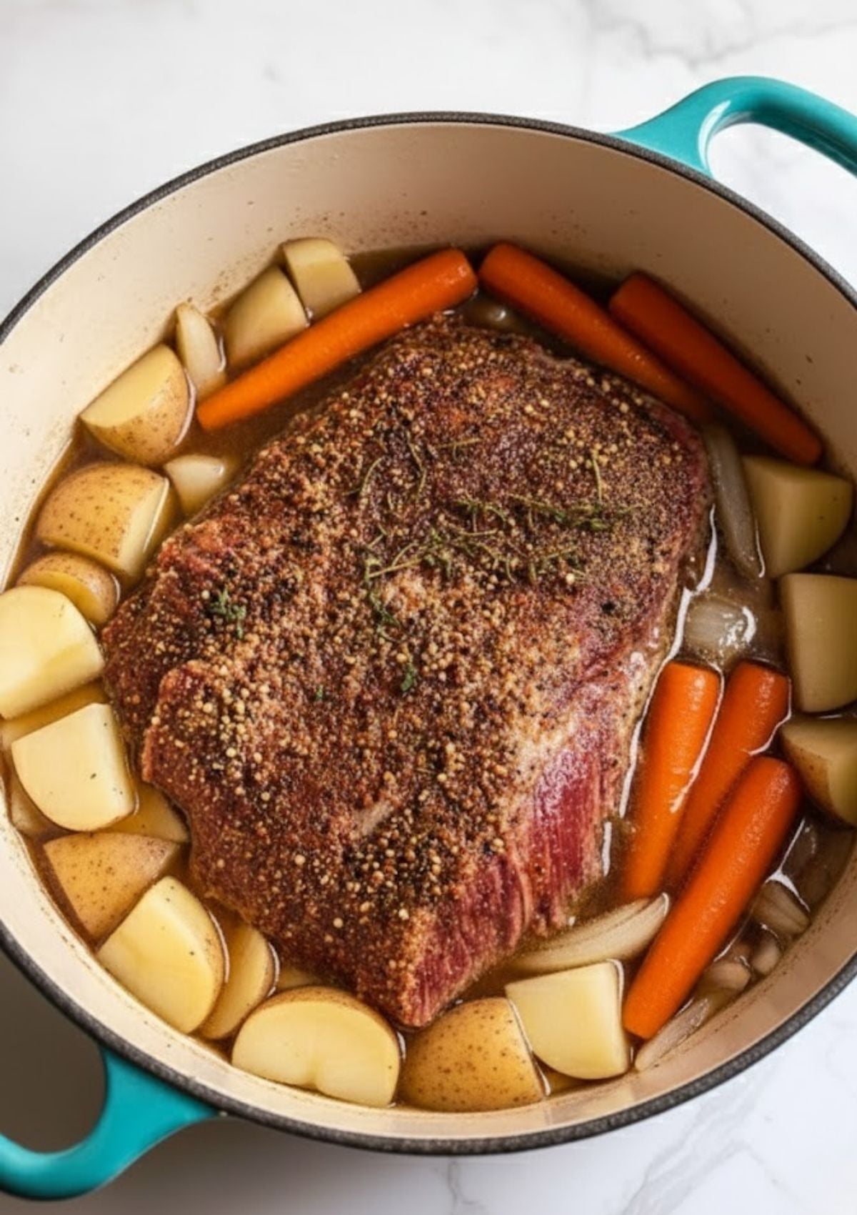 Corned beef brisket in a Dutch oven with chopped carrots, potatoes, and onions, ready to be slow-baked for the most tender results.
