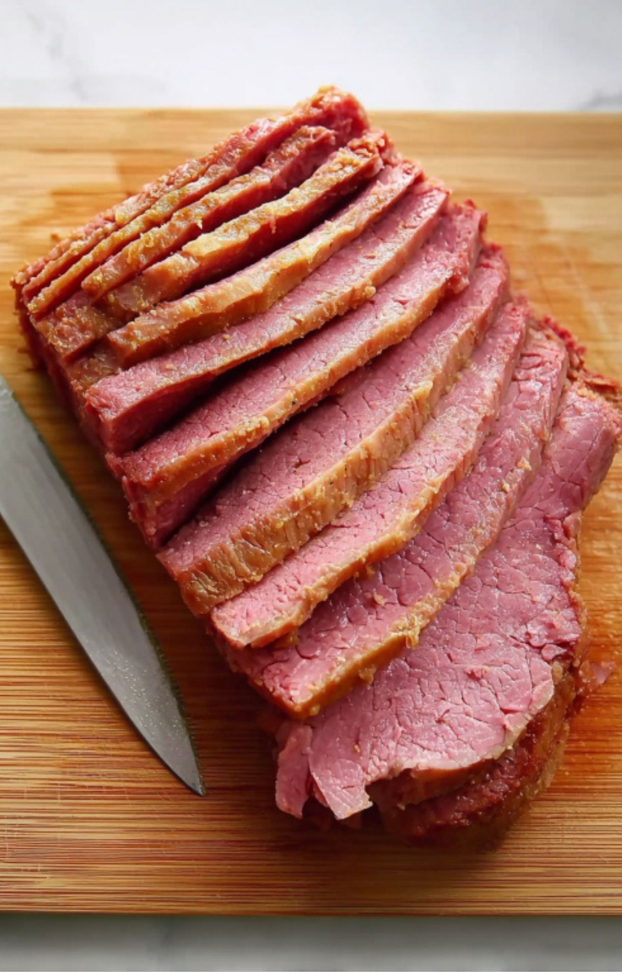 Sliced Guinness braised corned beef on a wooden cutting board with carving knife, juicy and ready to serve