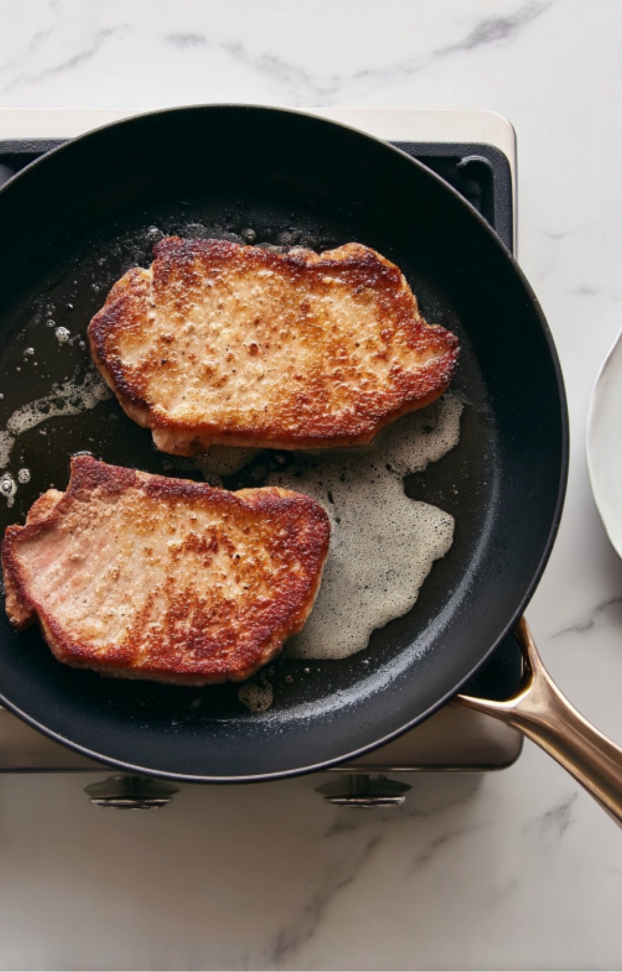 Two veal cutlets sizzling and turning golden in a skillet with melted butter, ready for a classic Italian scallopini dinner.
