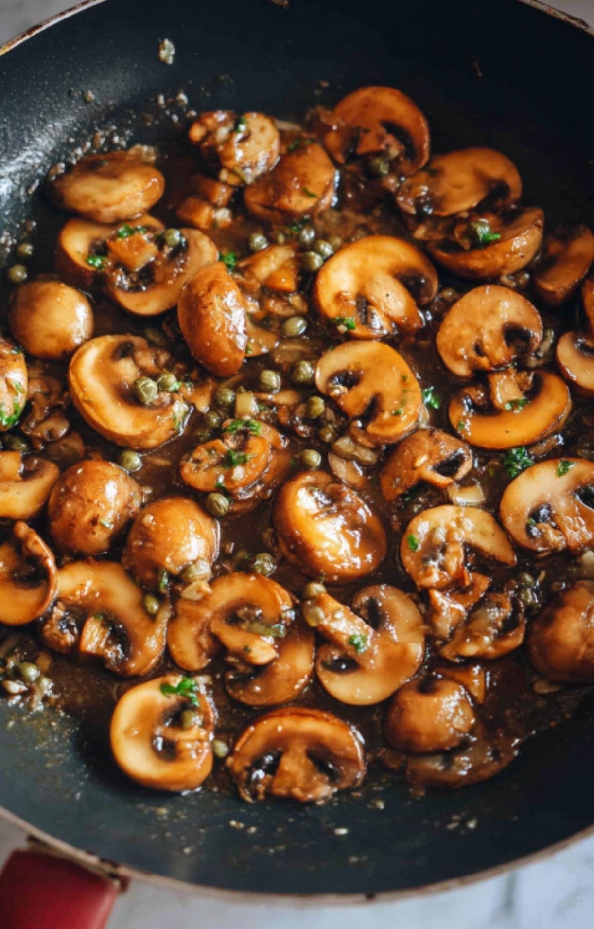 Several veal scallopini cutlets simmering in a skillet, covered in mushroom white wine sauce and garnished with parsley. Classic Italian skillet dinner ready to serve.