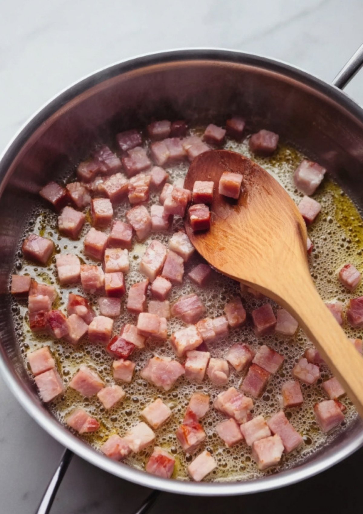 Pancetta cubes sizzling in olive oil in a skillet, stirred with a wooden spoon for braciole filling.